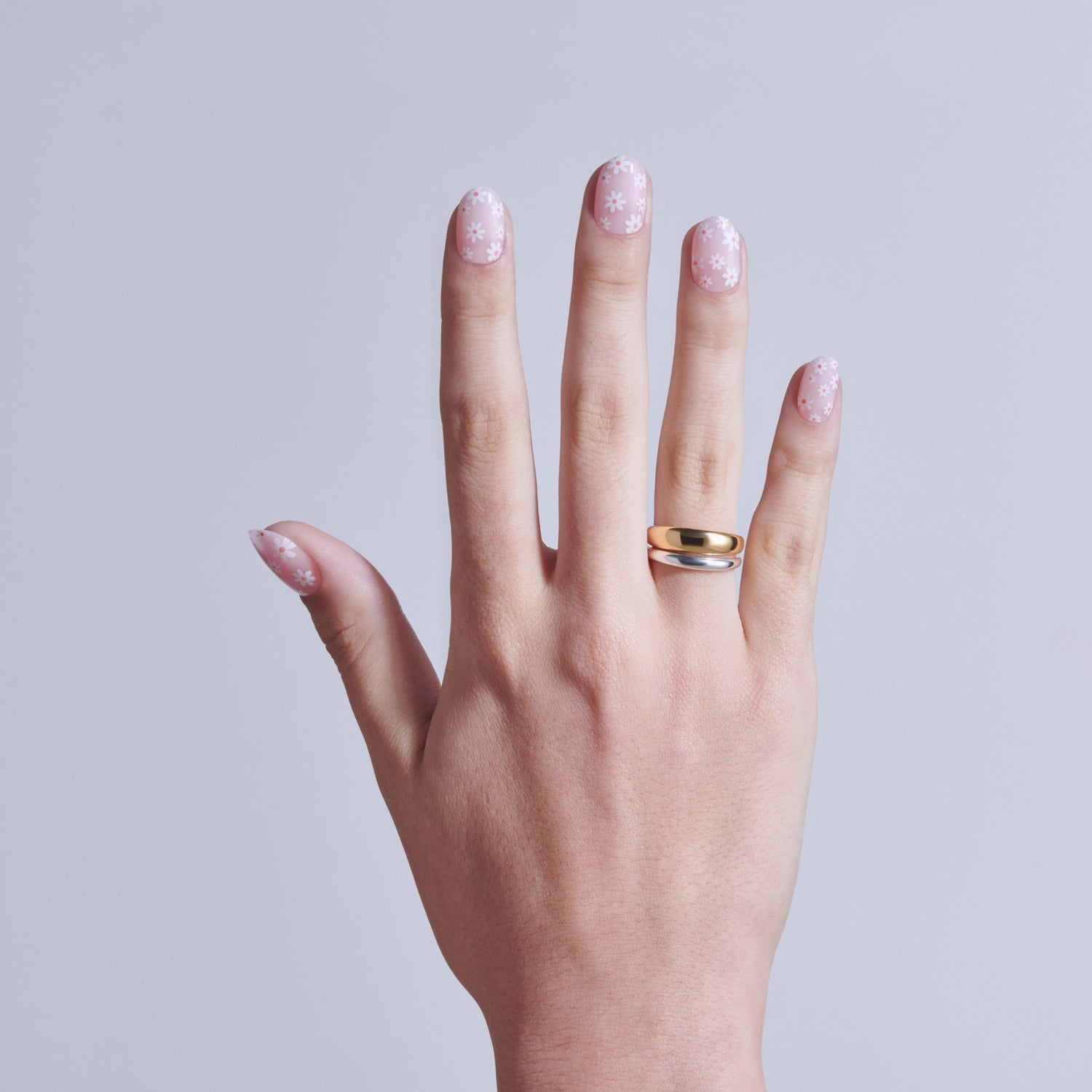Hand displaying manicured nails with pink glitter polish and gold/silver band ring.