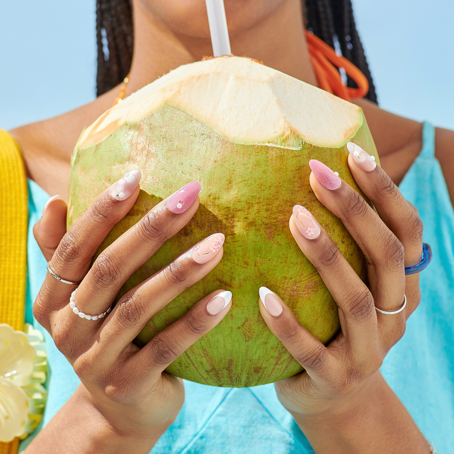 Person holding a green coconut with a straw, wearing colorful clothing against a blue background