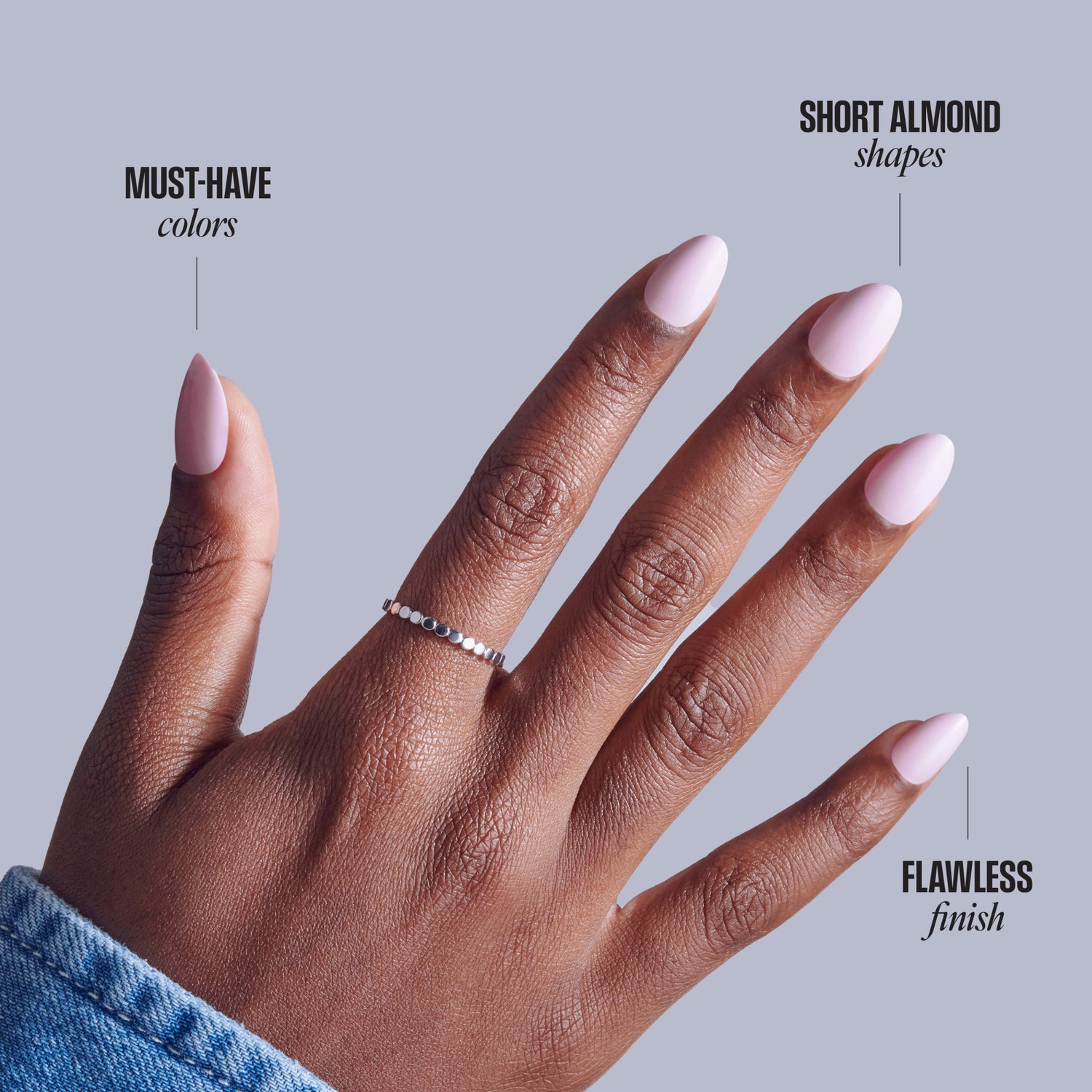 Short almond nails with pink polish on dark skin tone hand against gray background.