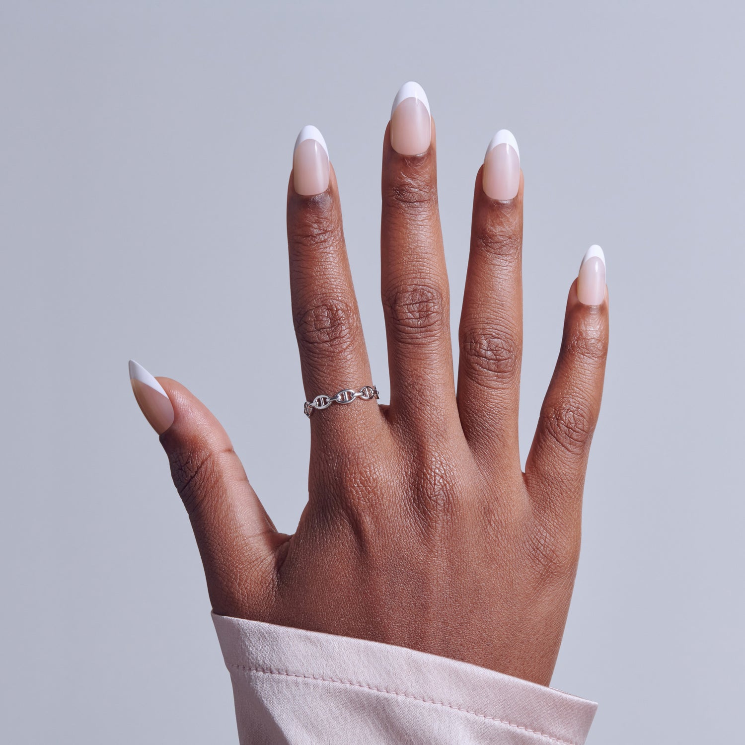 Hand displaying white French tip nails and silver chain ring against gray background.