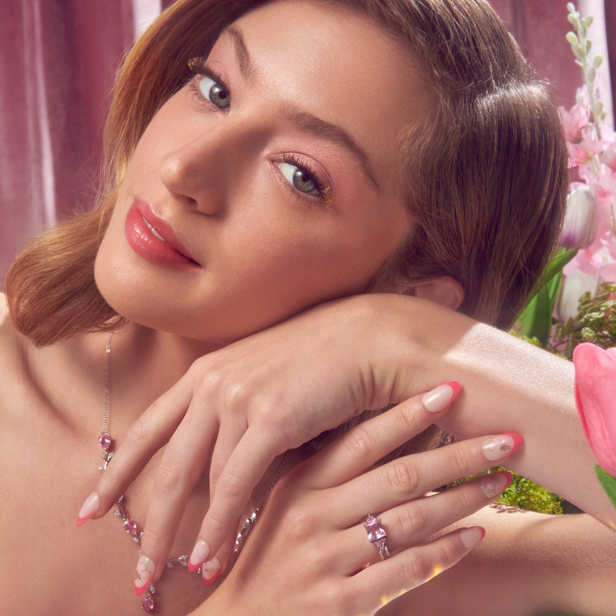 Woman with red and white ombre nails wearing pink jewelry against floral background