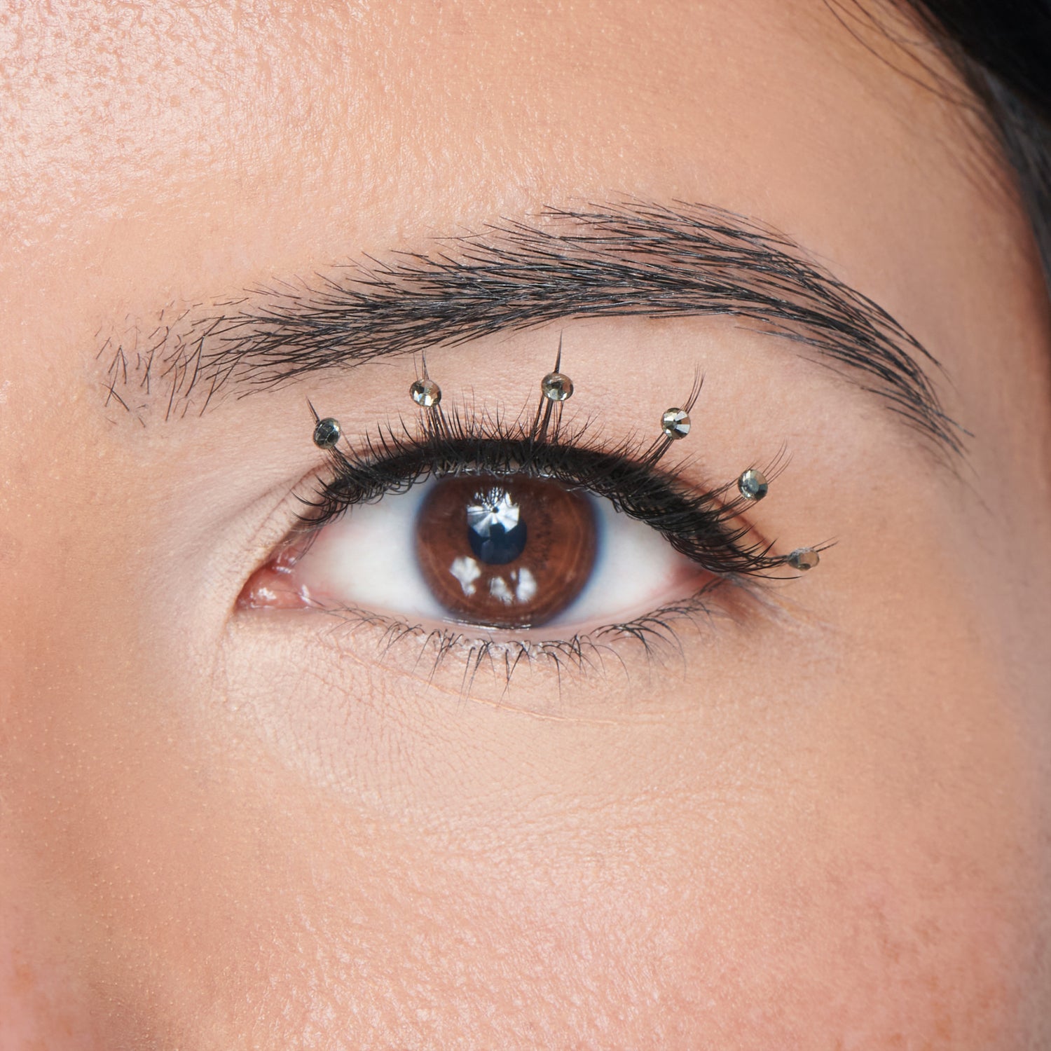 Close-up of a brown eye with black decorated false lashes featuring small clear gem stickers spaced along the upper lash line for a flapper girl look.