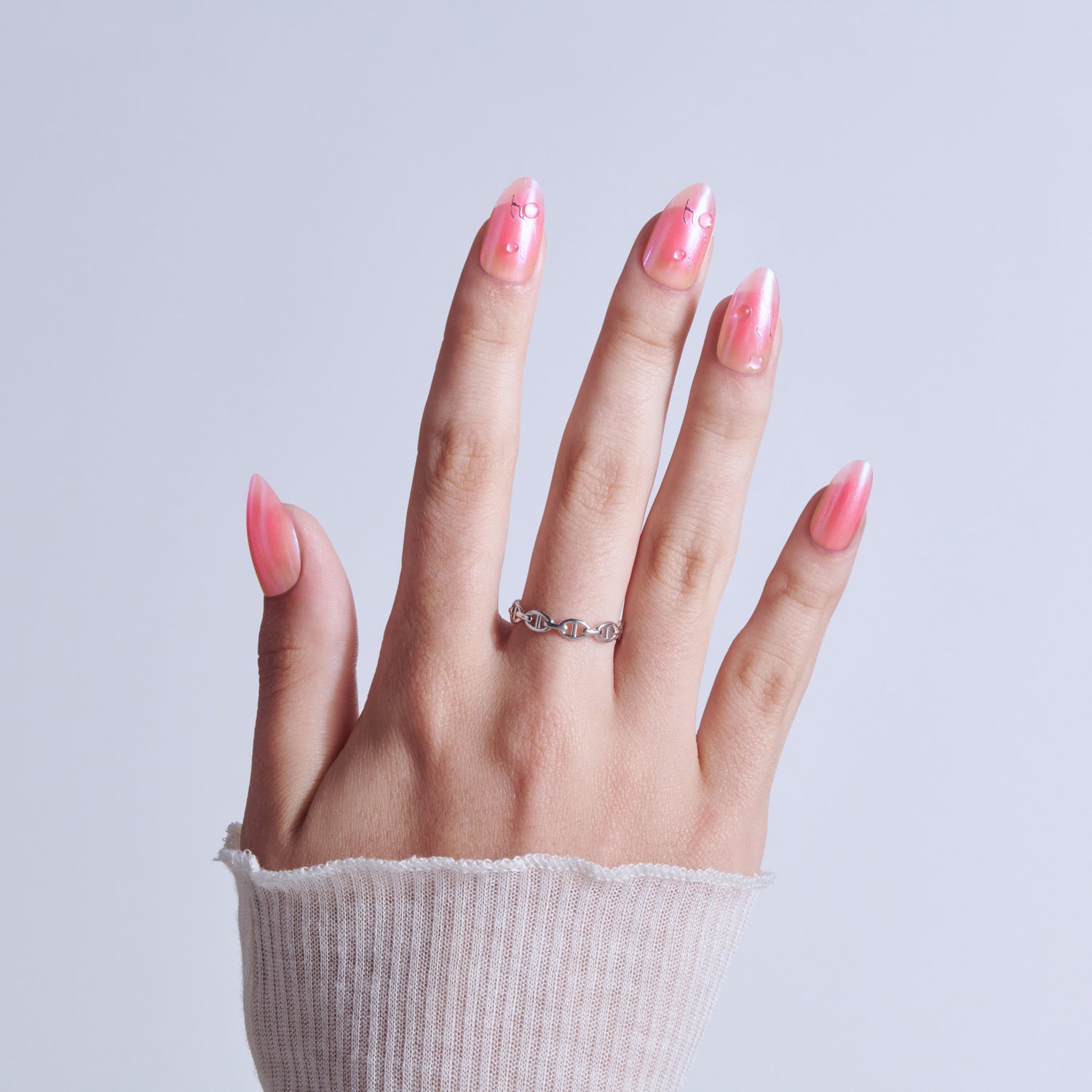 Hand with pink almond nails and silver chain ring against white background