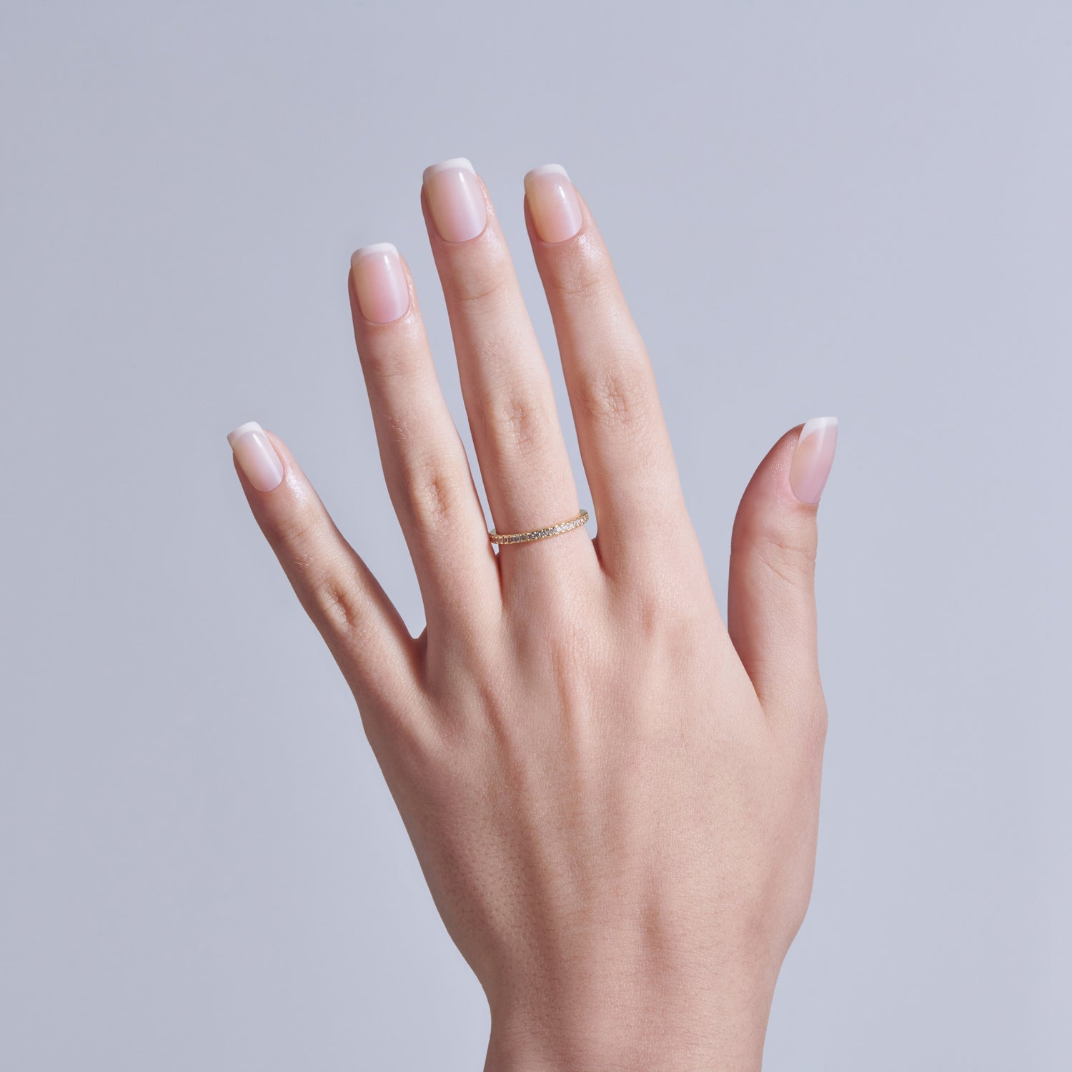 Hand displaying classic French manicure with gold ring on neutral background.
