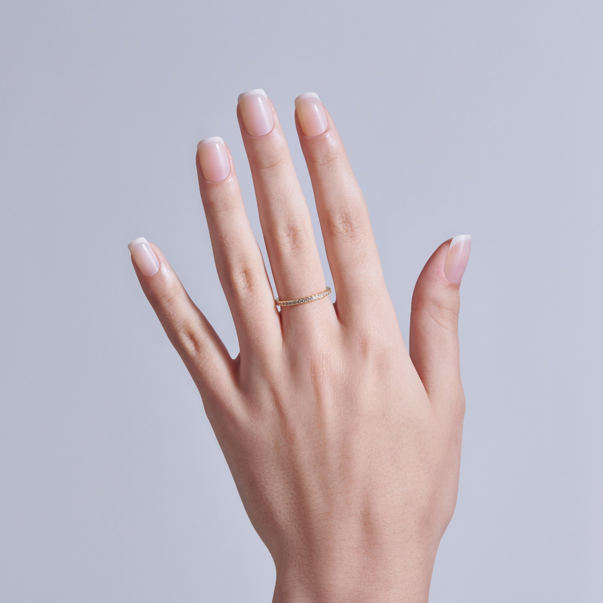 Hand displaying classic French manicure with gold ring on neutral background.