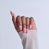 Hand with pink ombré manicure and almond nails wearing white knit sleeve against light background.