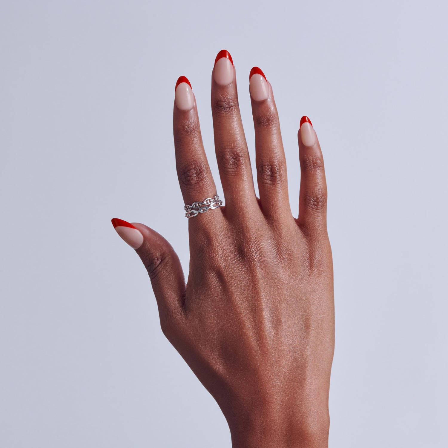 Hand with red and white ombre nails wearing silver chain ring against white background.