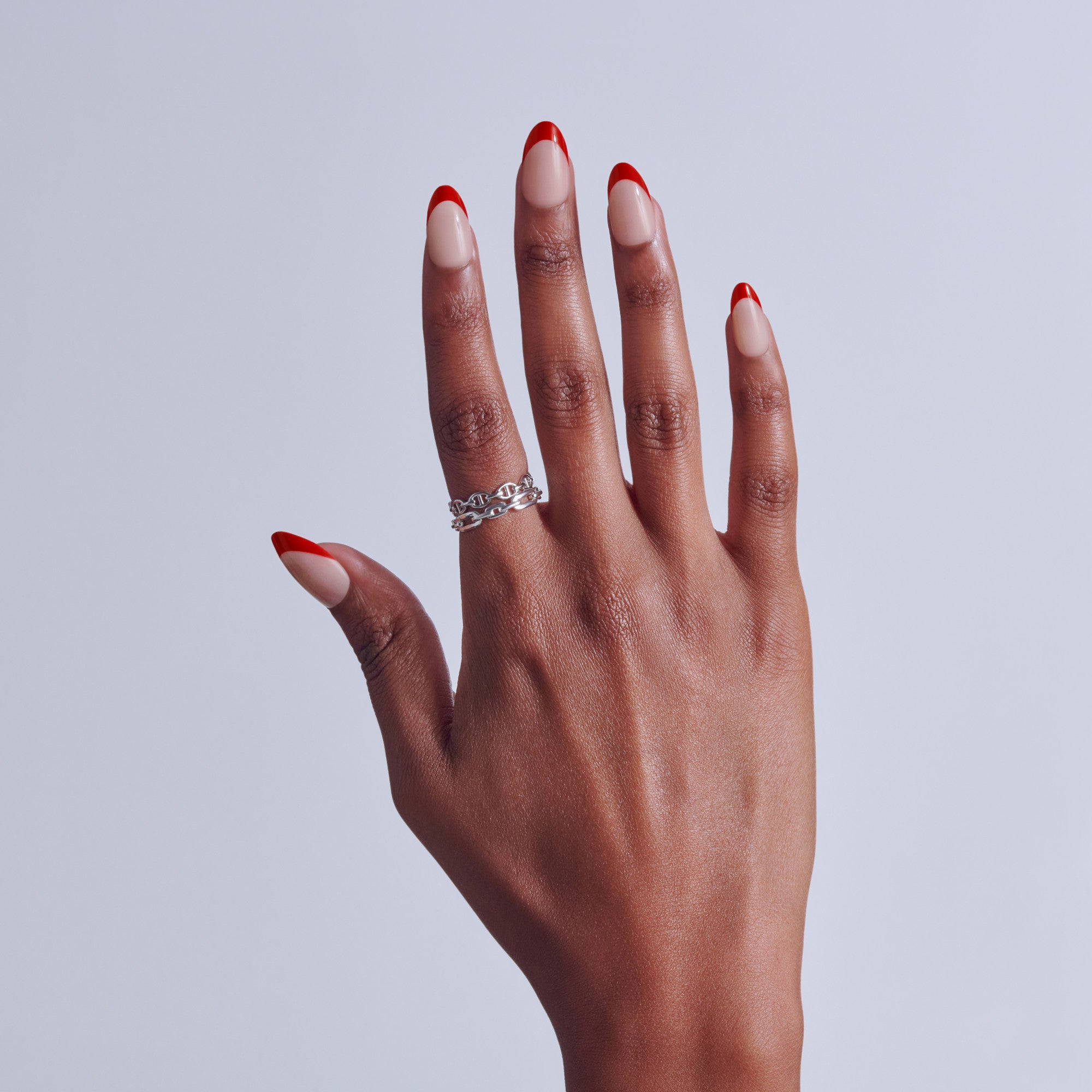 Hand with red and white ombre nails wearing silver chain ring against white background.
