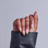 Hand with almond nails featuring pink base and gold tips, wearing gold ring, holding black leather clutch.