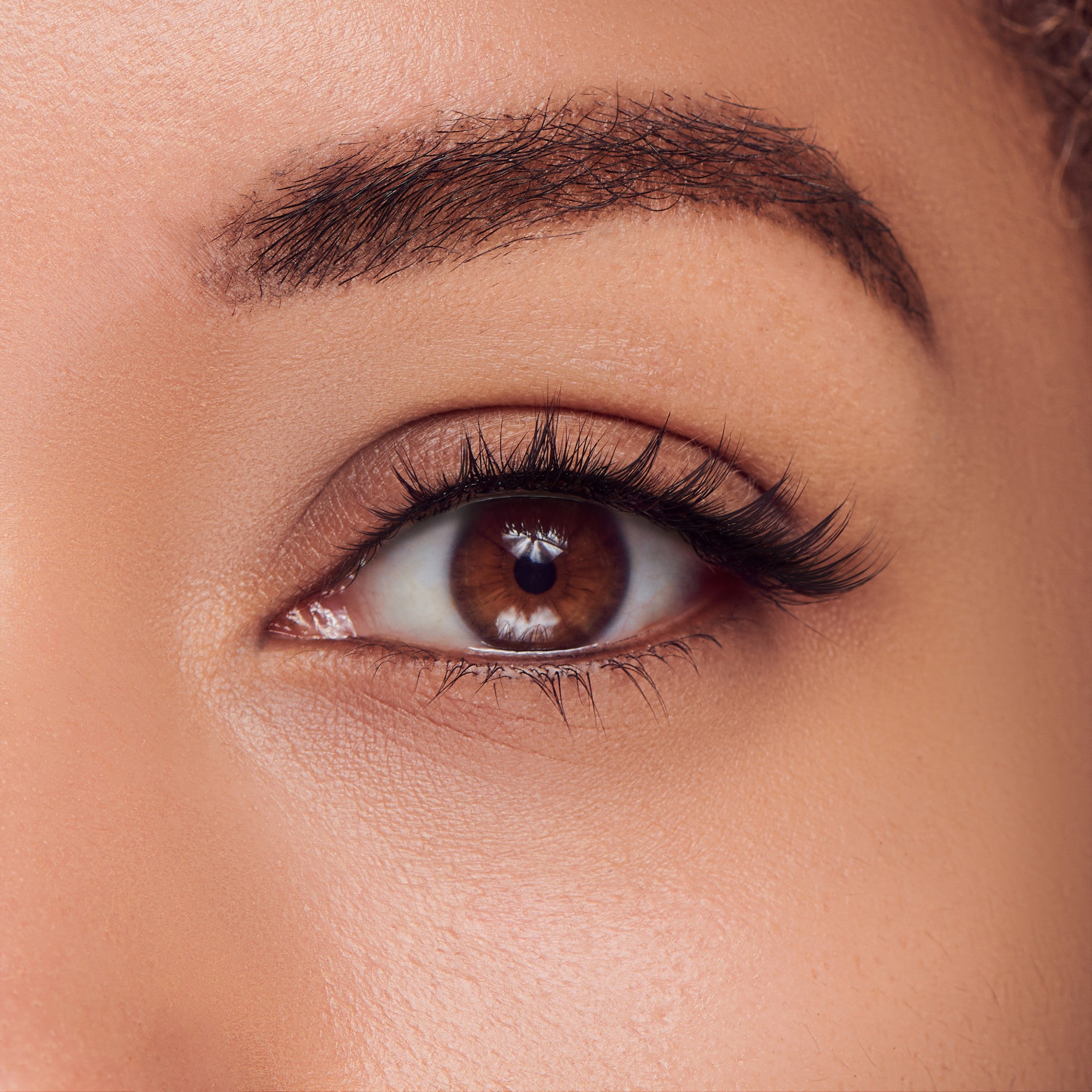 The image features a close-up of a human eye, showcasing a rich brown iris and a well-defined pupil. The eyelashes are long and prominent, enhancing the eye&
