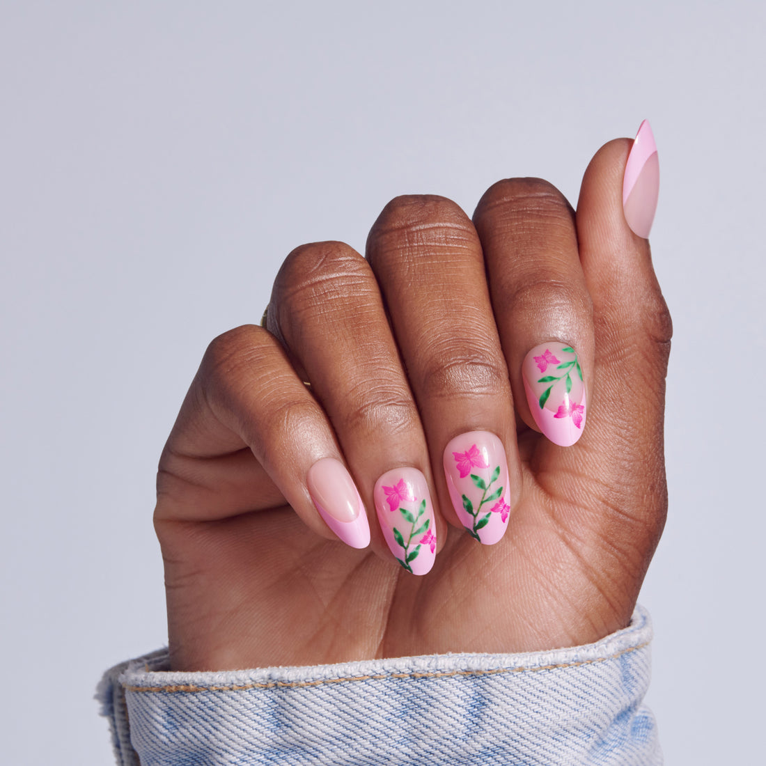 Pink almond nails with floral design and green leaf details on brown skin tone.