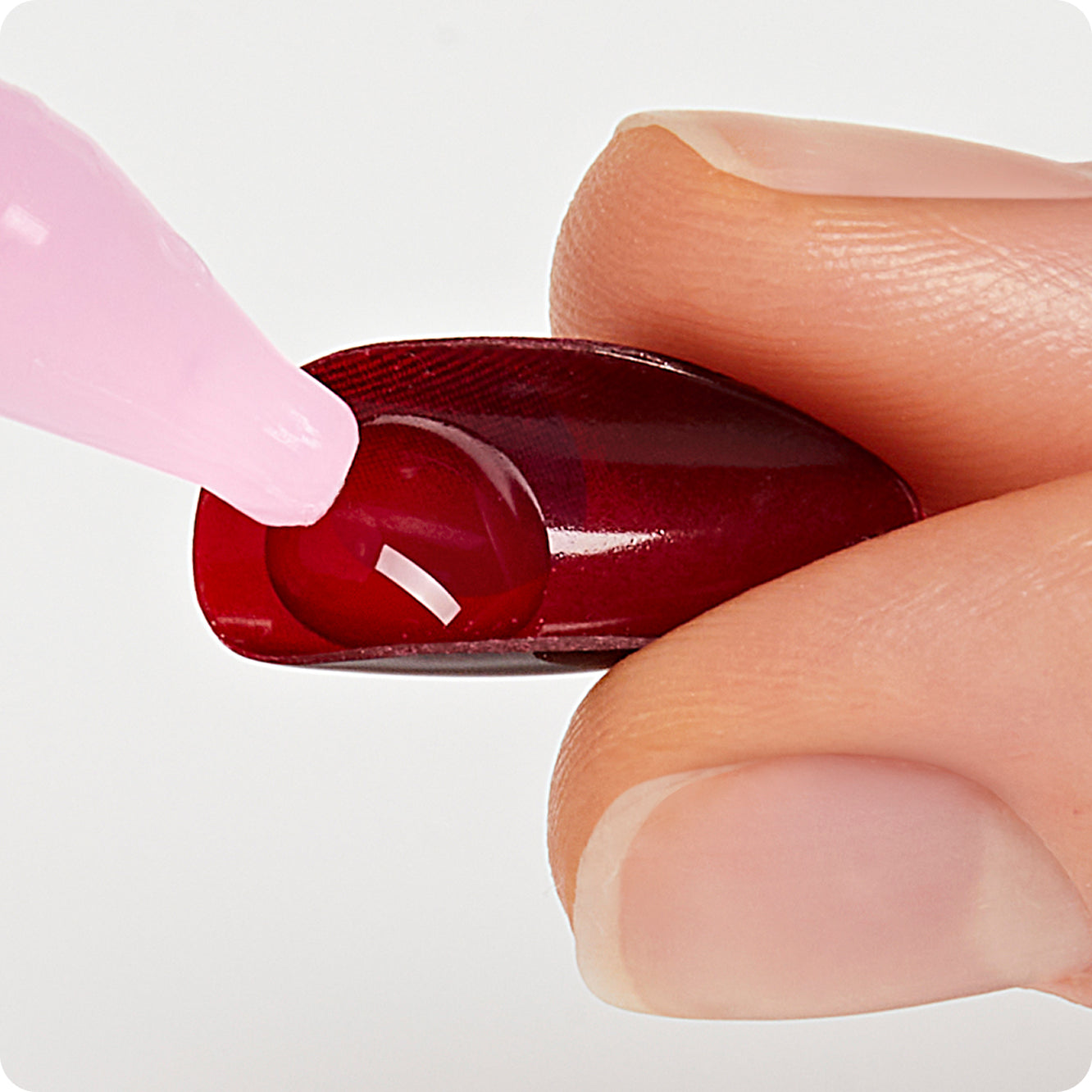 Deep burgundy nail polish being applied to a fingernail with a pink brush.