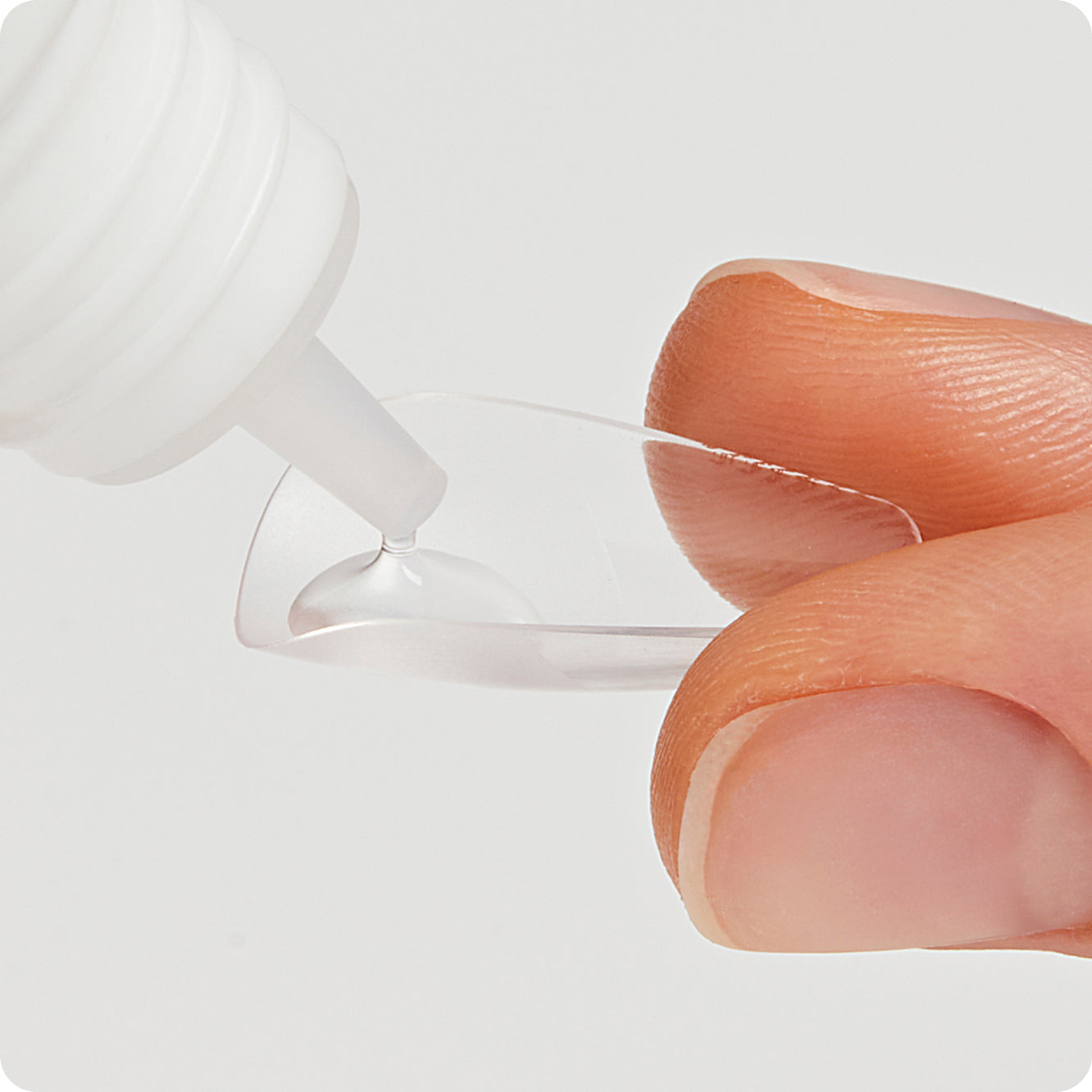 Close-up of a clear nail held between two fingers and getting applied nail glue.