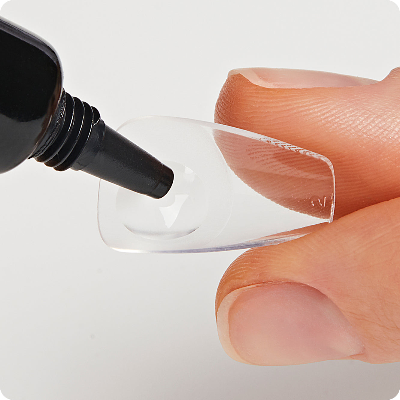 Person applying a clear gel or adhesive to a small nail with a black applicator.