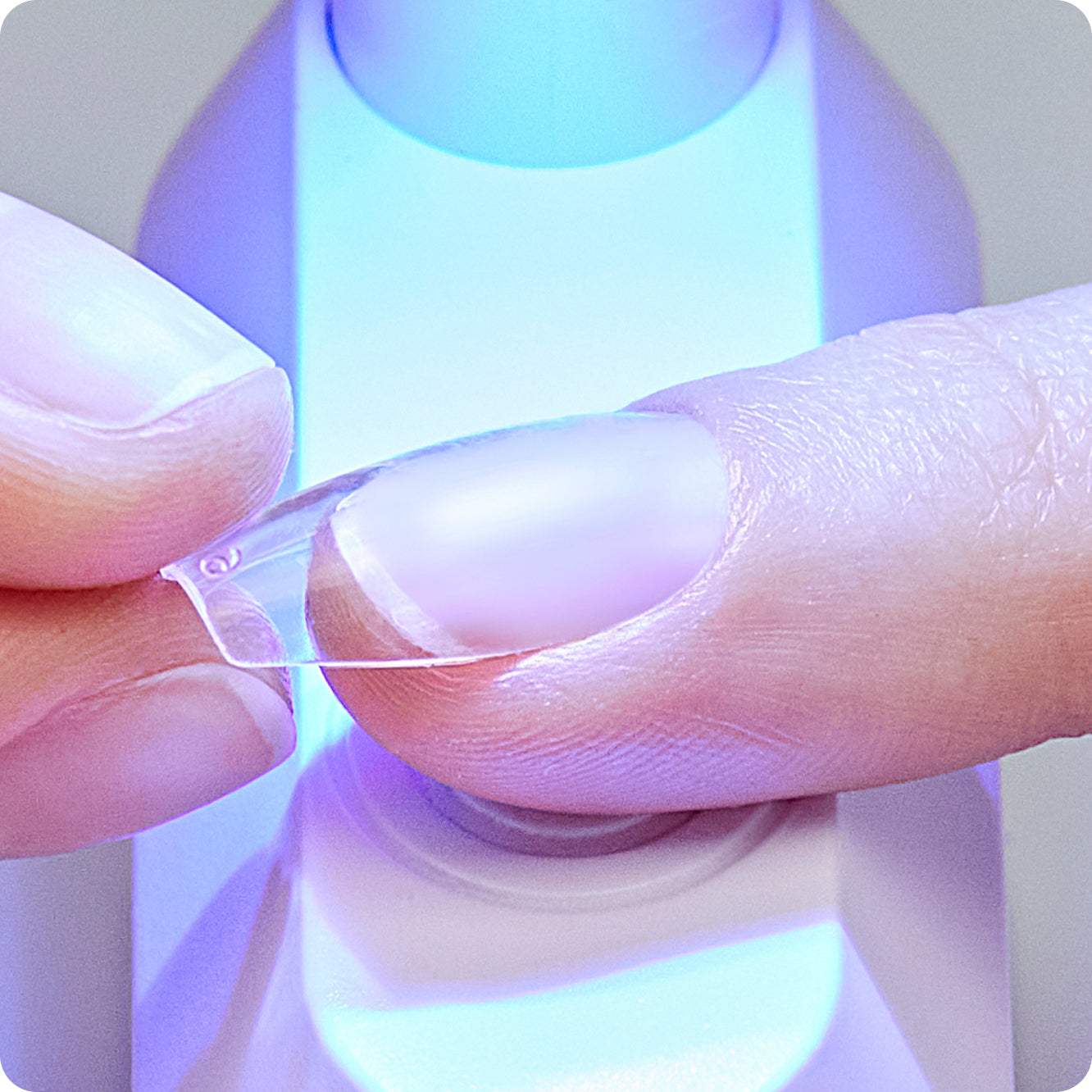 Close-up of a person holding a clear plastic nail with a small lamp curing the bonder