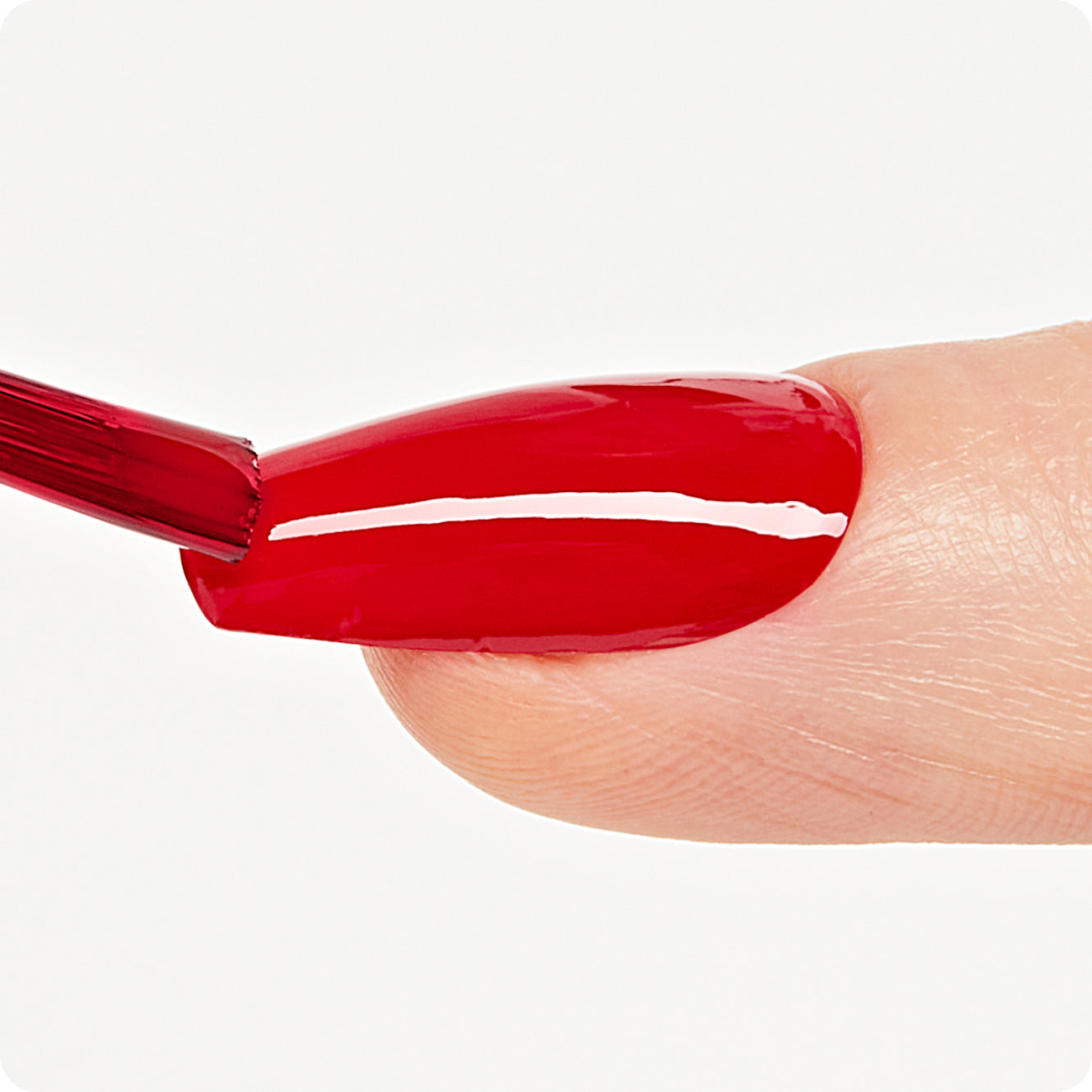 Close-up of a nail being painted with red nail polish on a white background