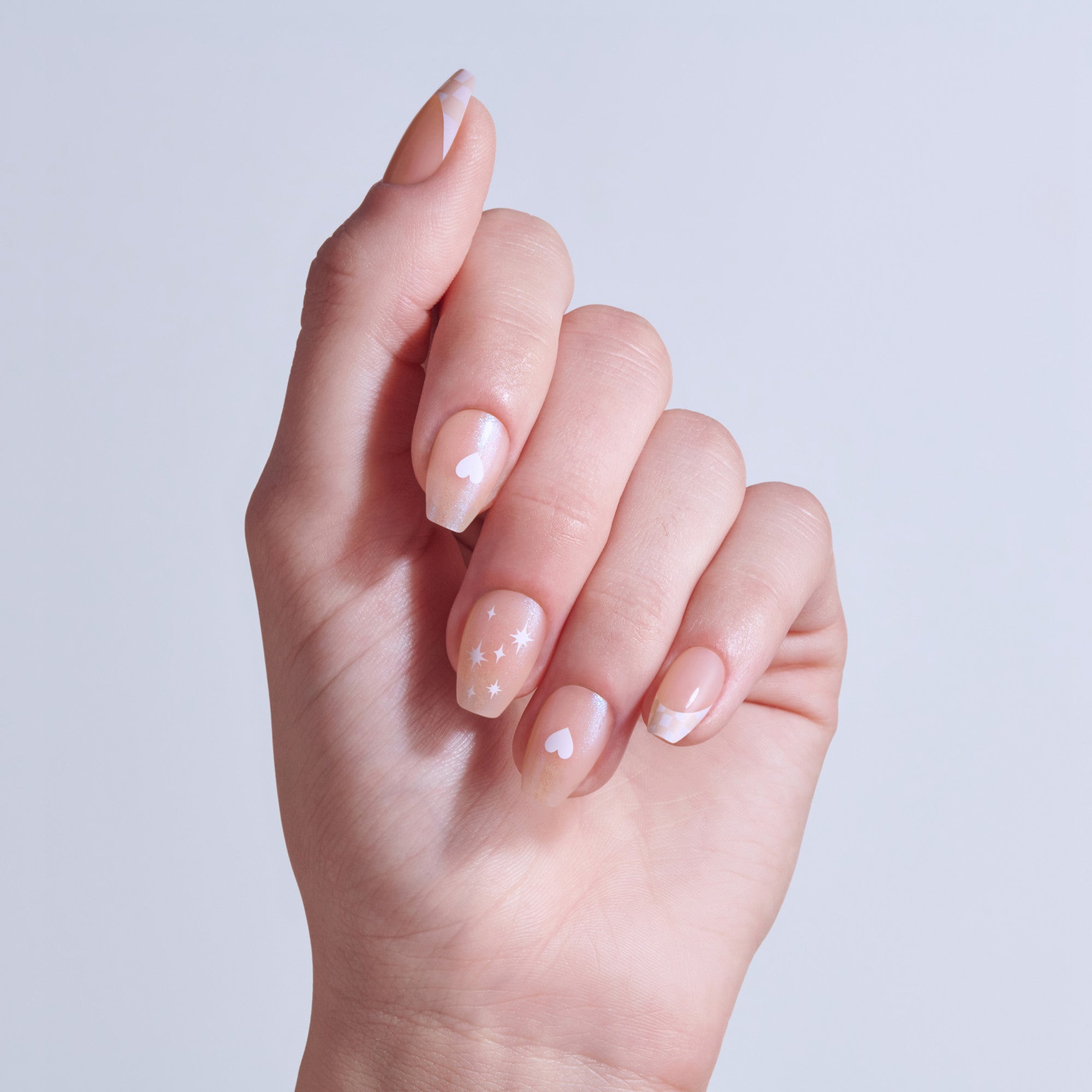 Hand displaying manicured nails with white stars and hearts on nude base polish.