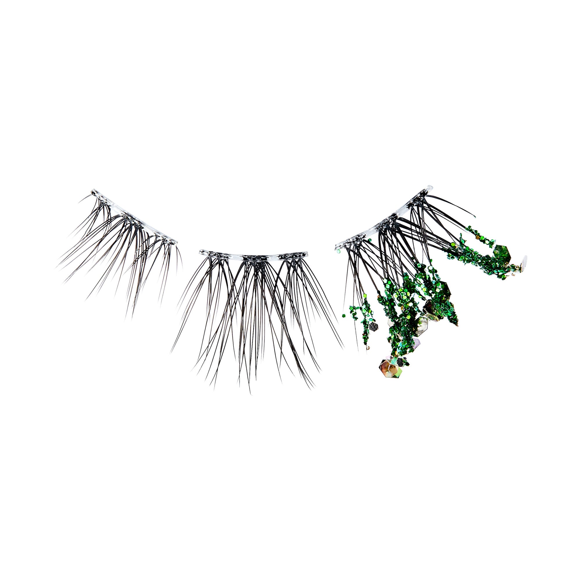 The image features a pair of false eyelashes, characterized by long, black strands that create a dramatic look. One of the lashes is adorned with green elements, resembling small pieces of foliage or moss, adding a unique and artistic touch to the overall design. The background is plain white, which emphasizes the contrast between the dark lashes and the vibrant green accents.