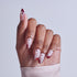 Almond nails with red and white floral nail art design on neutral background.