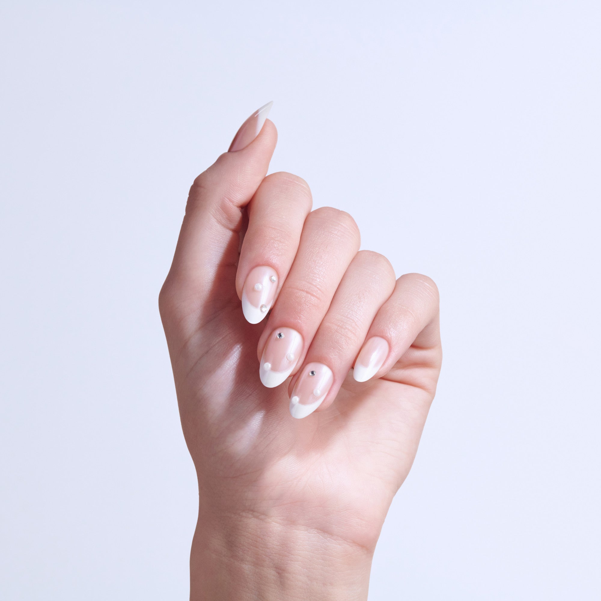 Hand displaying manicured nails with white and pink ombre design and small rhinestone accents.