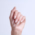 Hand displaying manicured nails with white and pink ombre design and small rhinestone accents.