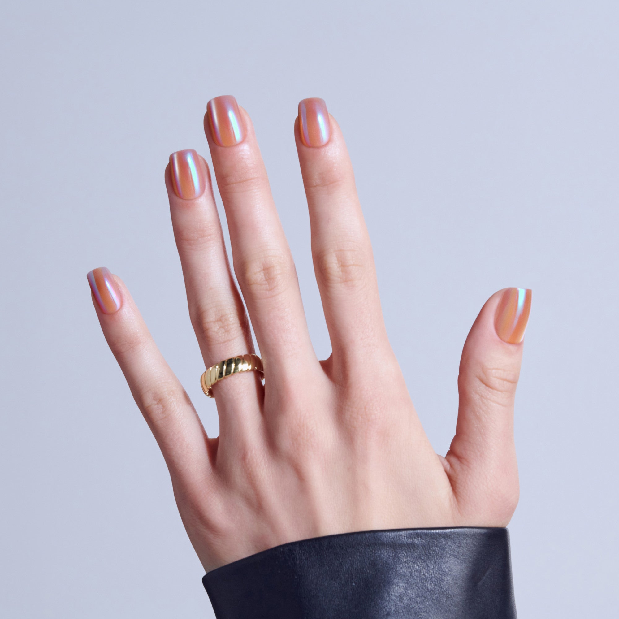 Hand displaying striped chrome nail art in warm metallic tones with gold ring.