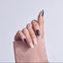 Hand displaying navy and white manicure with decorative nail art on beige fabric background.