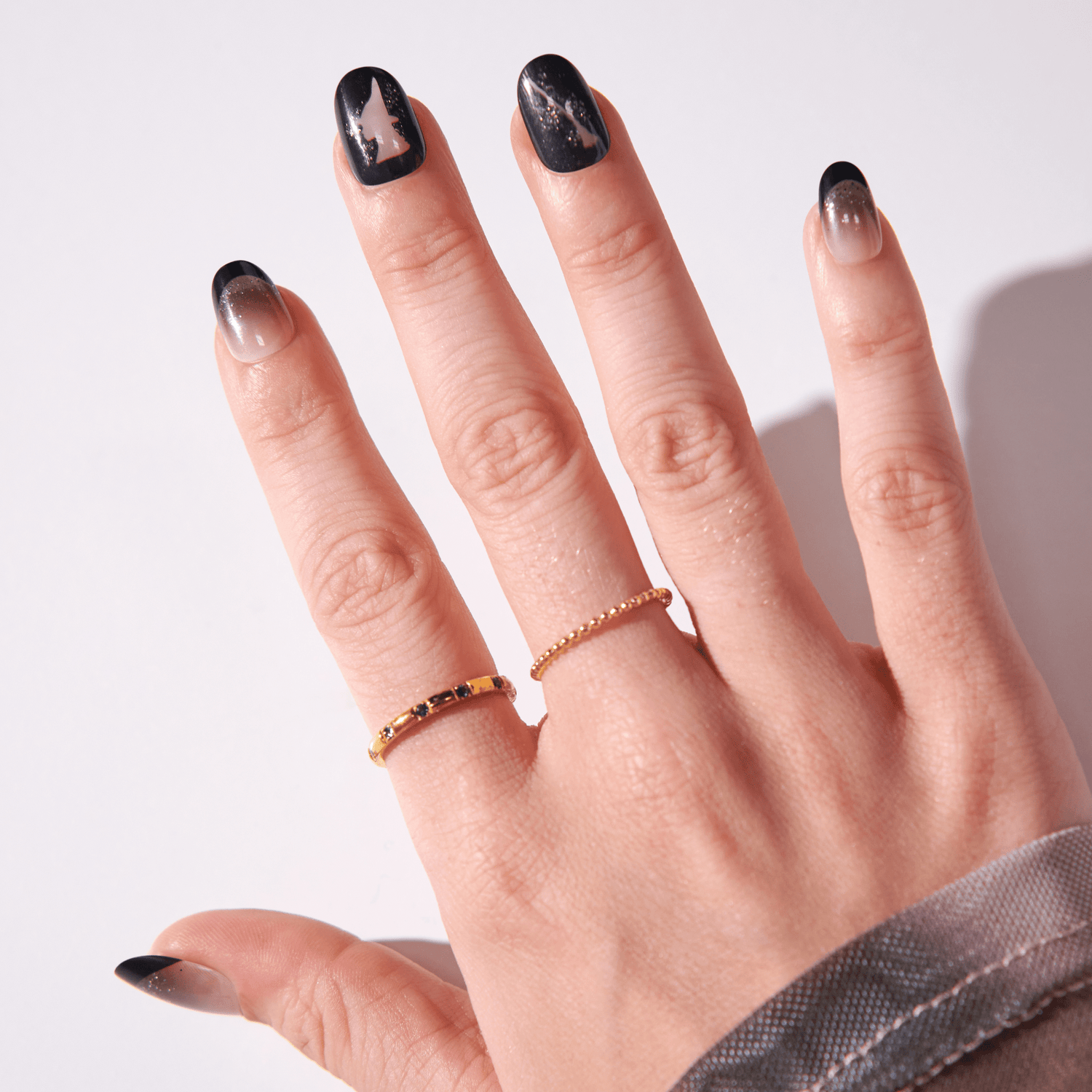 Hand displaying black marble nail art with gold accent rings