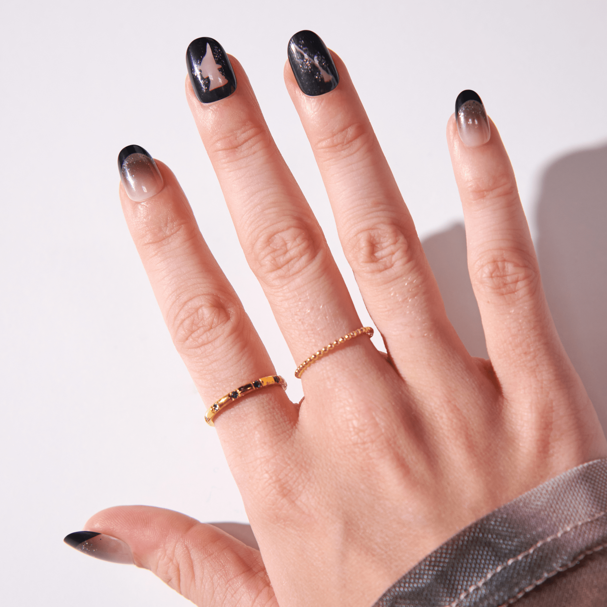 Hand displaying black marble nail art with gold accent rings