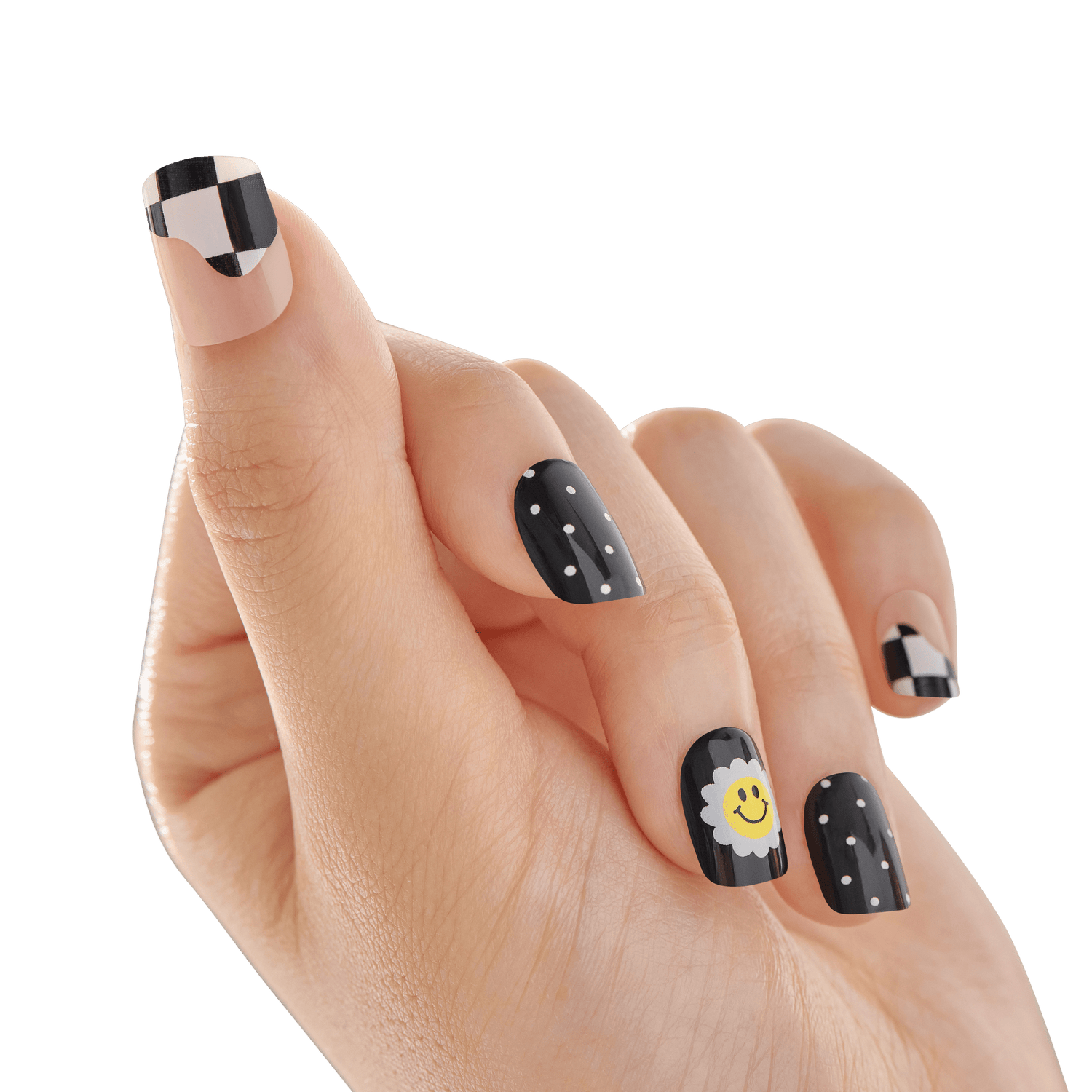 The image shows a close-up of a hand with manicured nails. The nails feature a variety of designs. The thumb and pinky nails have a black and white checkered pattern. The index and ring nails are painted black with small white polka dots. The middle nail is black with a white flower and a yellow smiling face in the center. The background is blurred, keeping the focus on the detailed nail art.