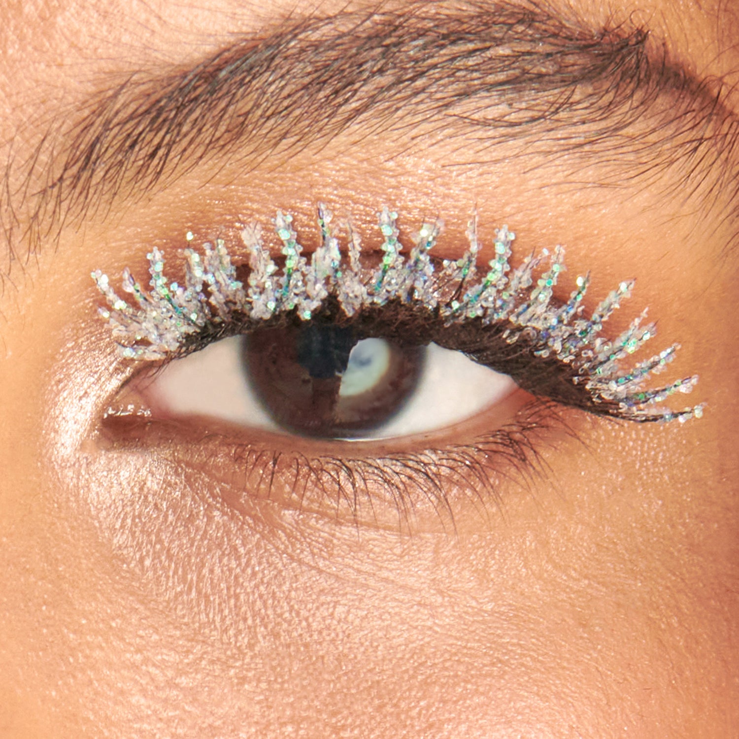 Close-up of eye with glittery silver and iridescent lashes and warm-toned eyeshadow.