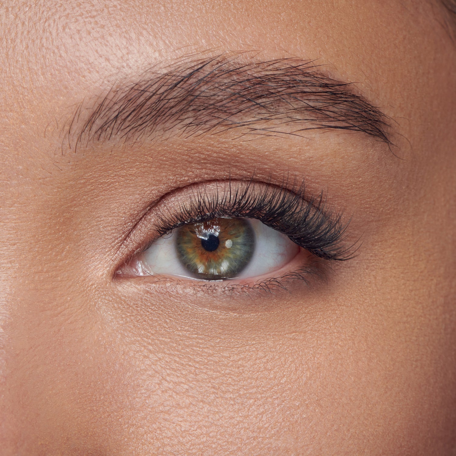Close-up of a greenish eye with individual black lash extensions applied, showing natural-looking volume and length on the upper lashes.