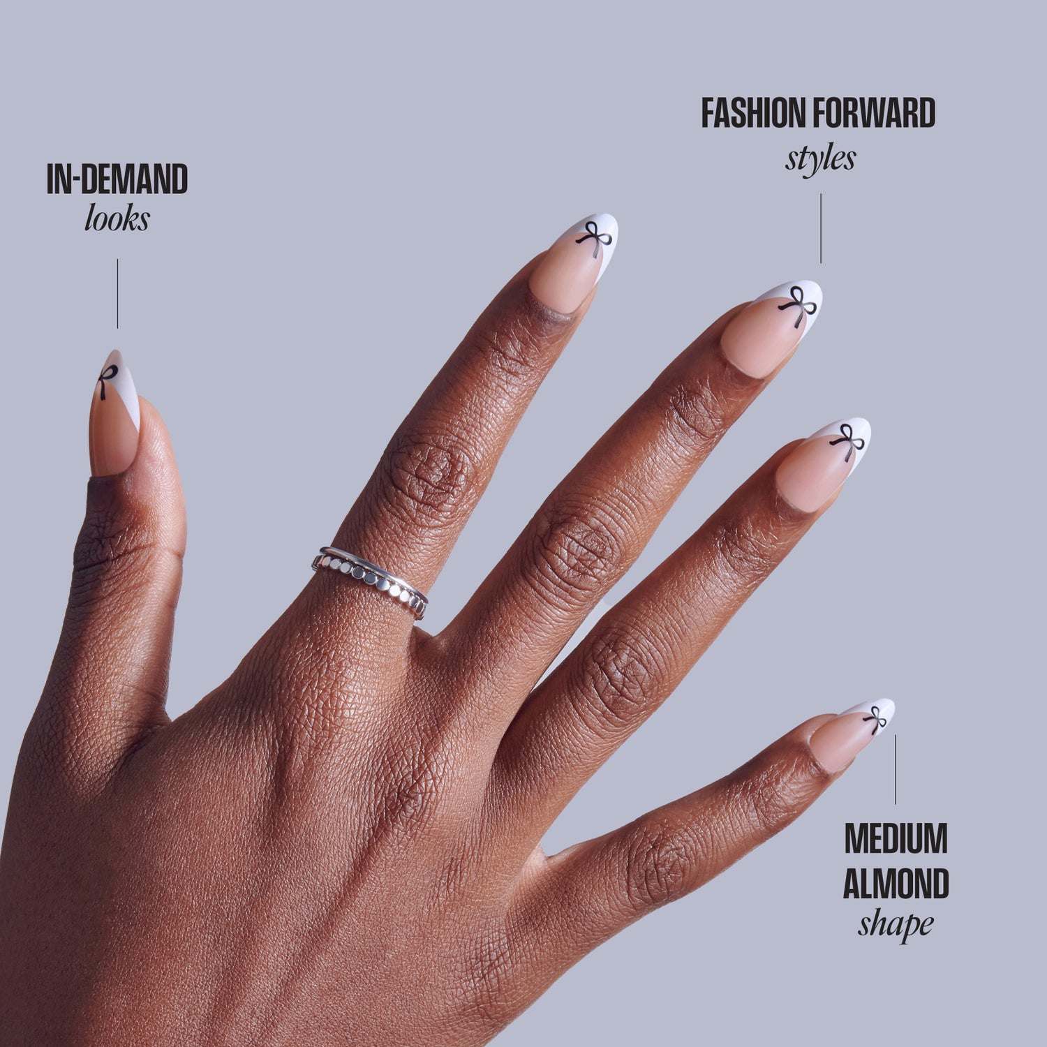 Hand displaying medium almond-shaped nails with bow designs and diamond ring against gray background.