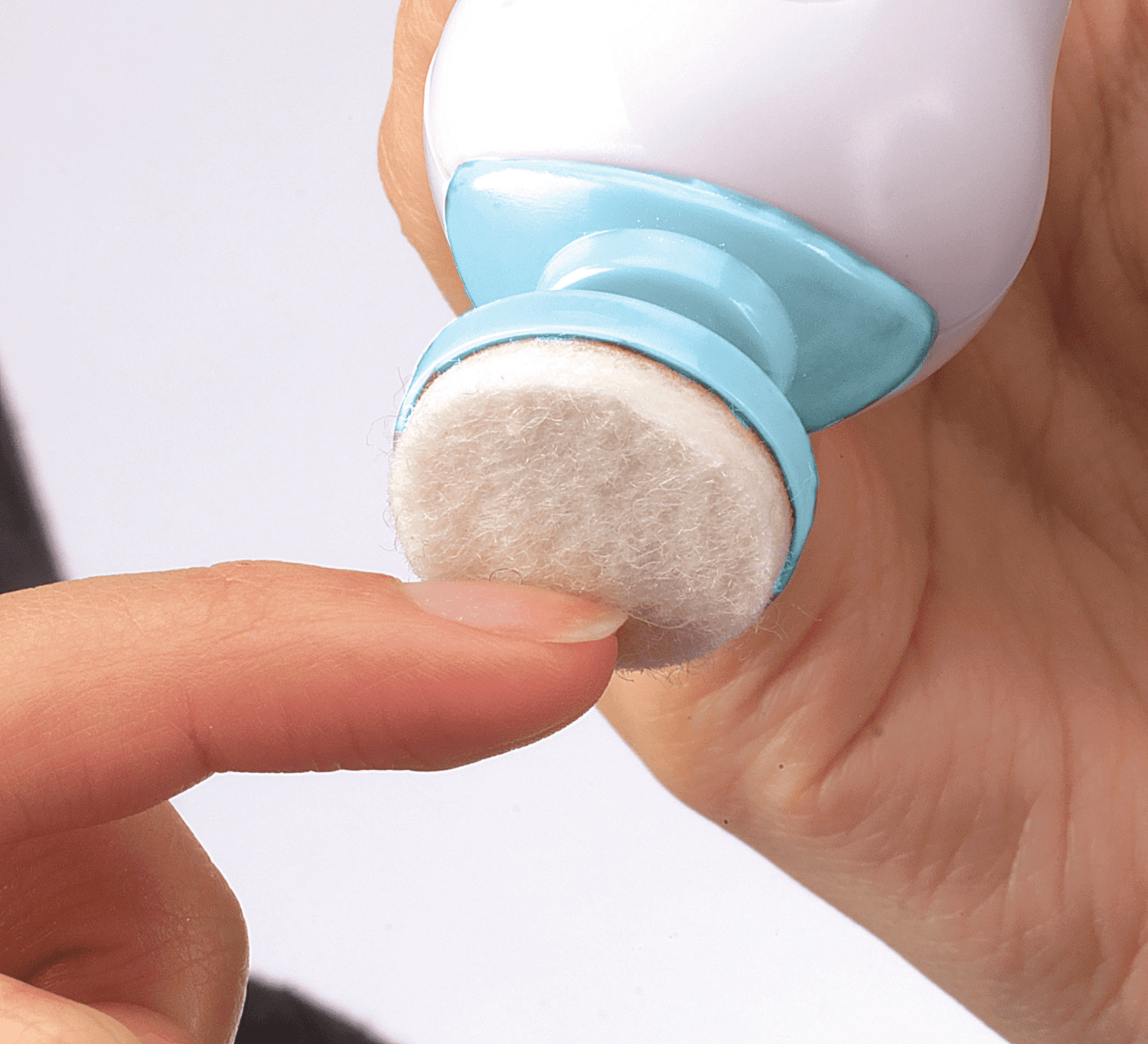 White and blue handheld electric nail file with a soft, round buffing tip, shown in use smoothing a fingernail on a light background.