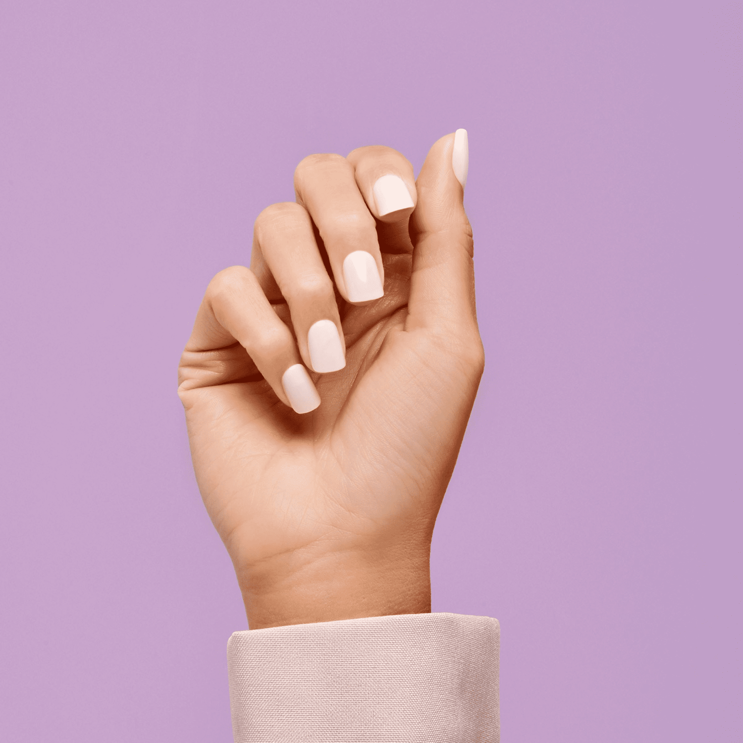 Hand with medium-length, squared pink press-on nails shown against a solid light purple background, wearing a pale pink long sleeve.