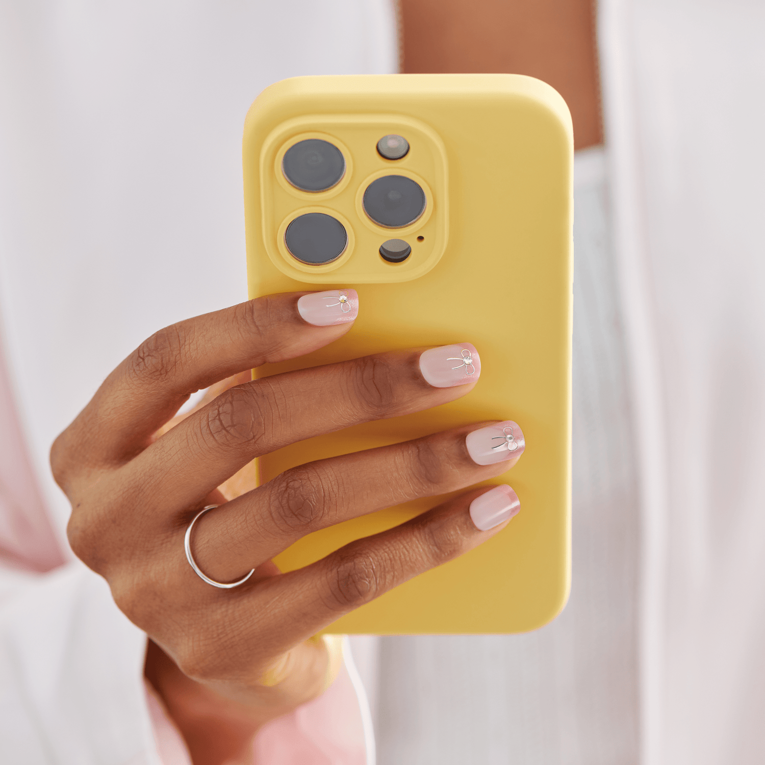 Yellow iPhone 14 Pro case held by hand with manicured nails and silver ring