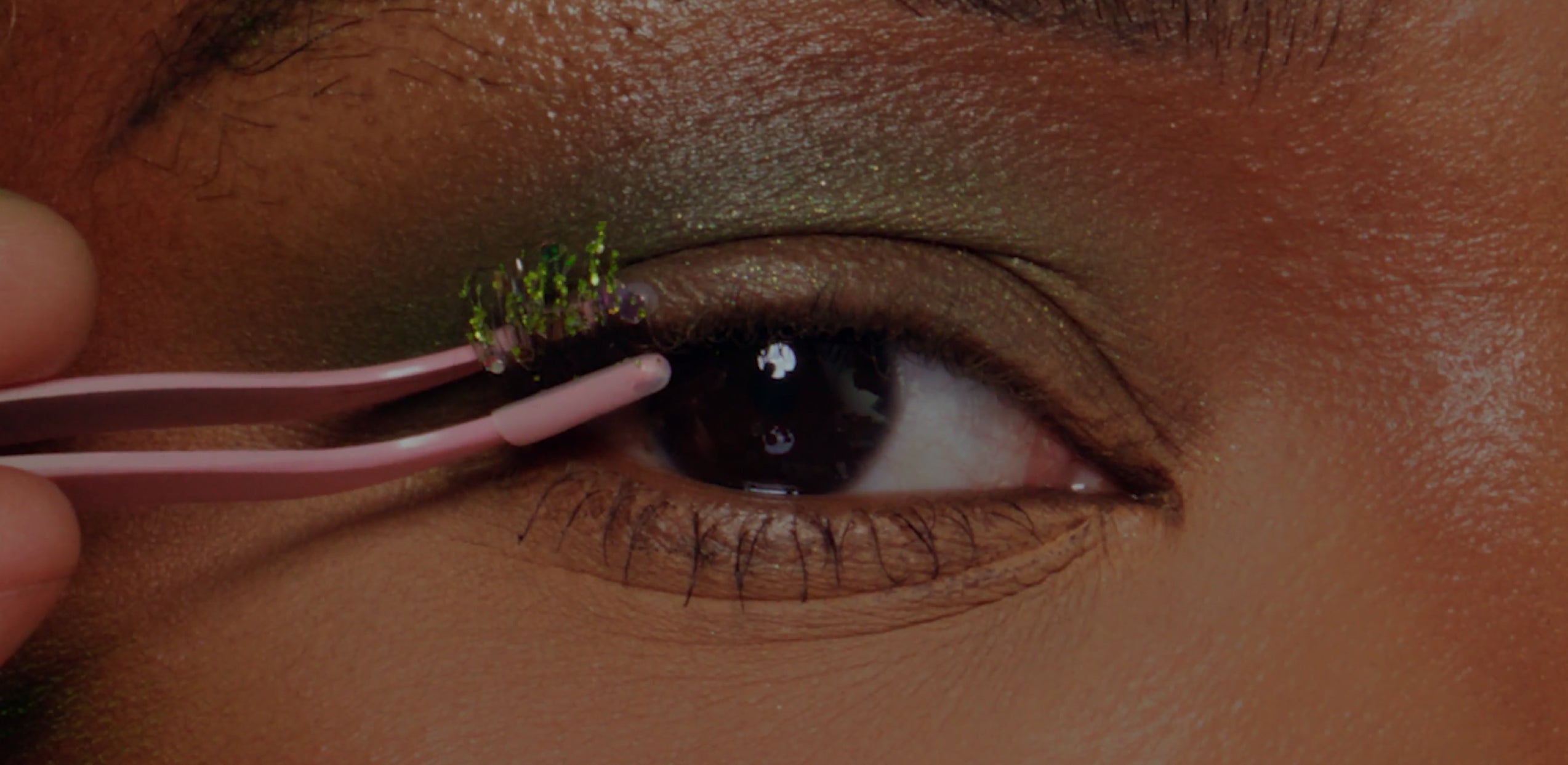 Close-up of eye with green eyeshadow and applicator applying false lashes