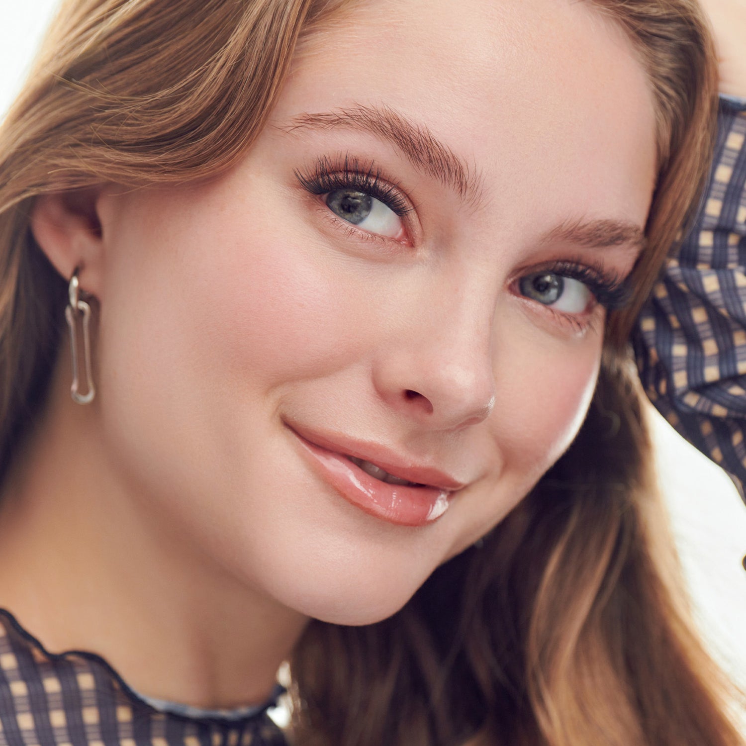 Woman with auburn hair, blue eyes, and natural makeup wearing hoop earrings and checkered shirt.