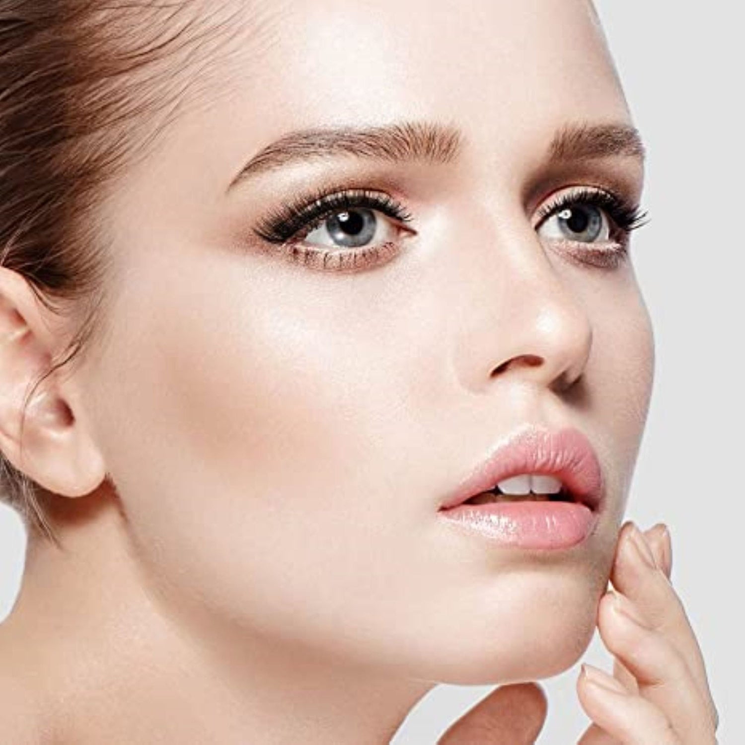 Close-up of a woman’s face with fair skin and blue eyes, wearing natural-looking false eyelashes that enhance her lashes’ length and volume.