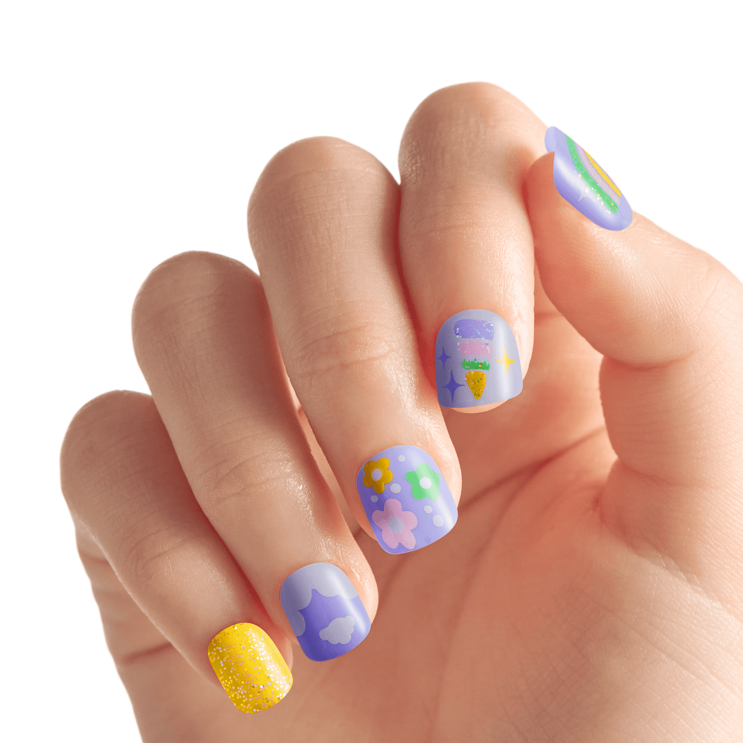 Hand with short press-on nails in pastel purple and yellow colors, featuring whimsical designs like flowers, clouds, a carrot, and sparkles.