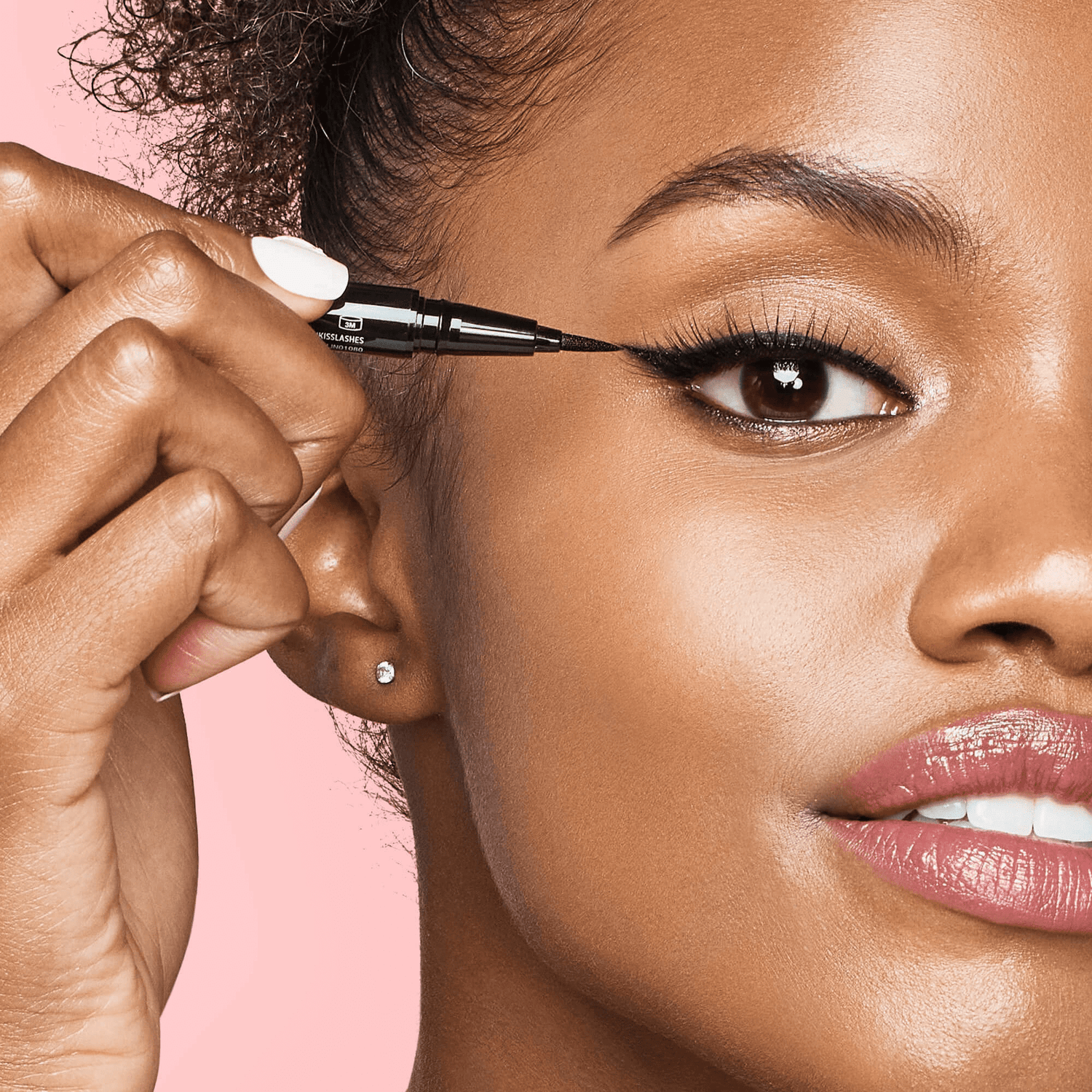 Close-up of a woman applying black KISS Lash GLUEliner eyeliner with a felt-tip applicator, highlighting precise winged eyeliner on her upper eyelid.