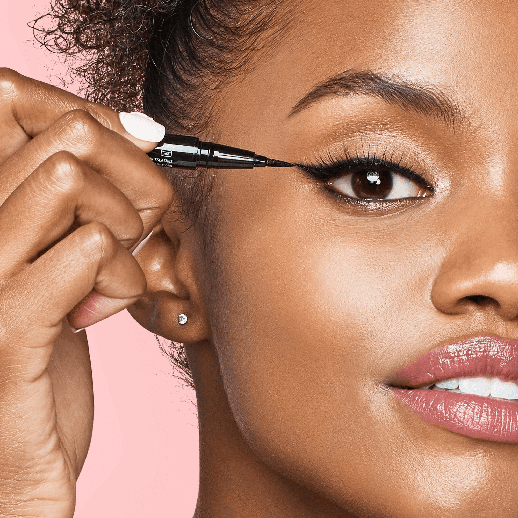Close-up of a woman applying black KISS Lash GLUEliner eyeliner with a felt-tip applicator, highlighting precise winged eyeliner on her upper eyelid.