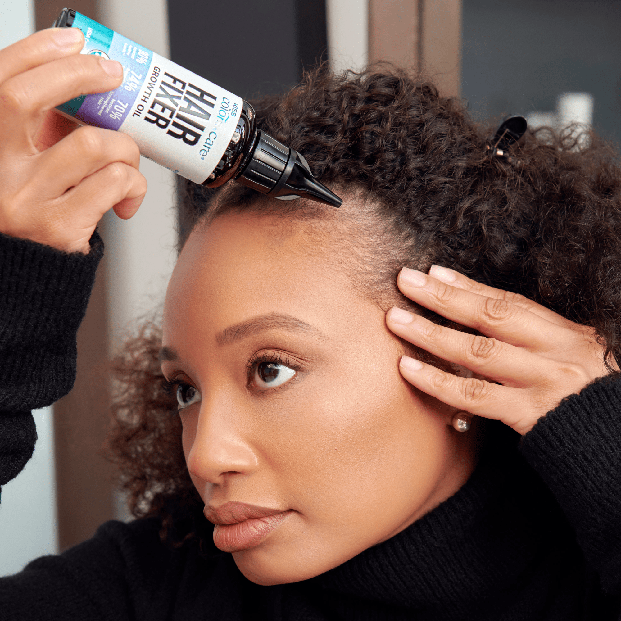 Woman with curly hair applying KISS Colors &amp; Care Hair Fixer Growth Oil to her scalp, promoting hair growth and care.
