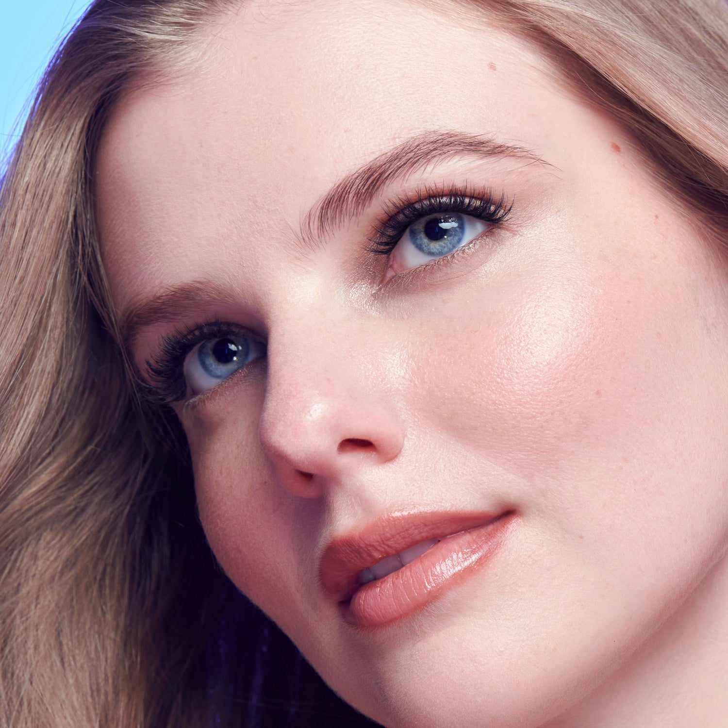 Woman with blue eyes, brown hair, and natural makeup against blue background