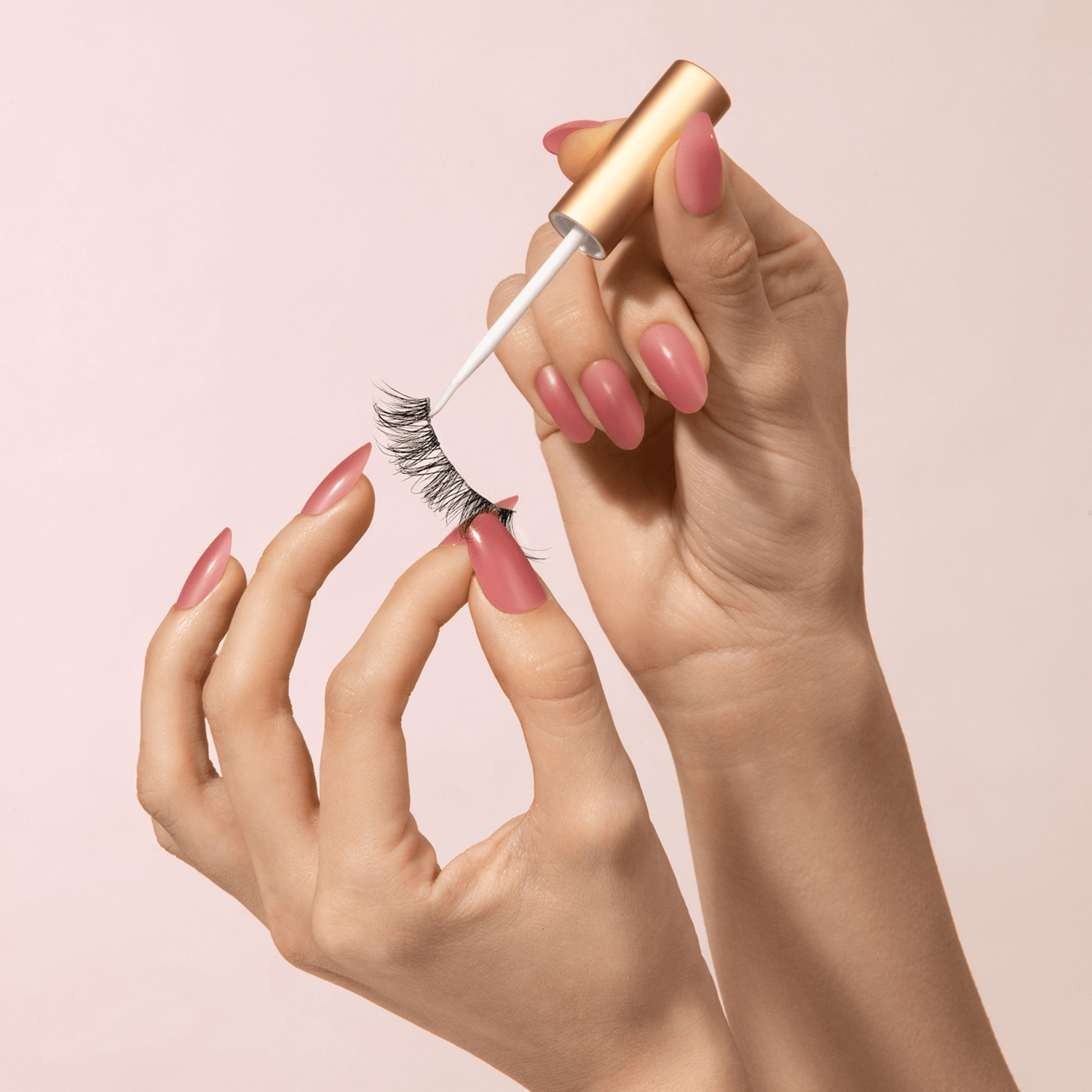Hand holding a eyelash curler with pink nails against a light pink background