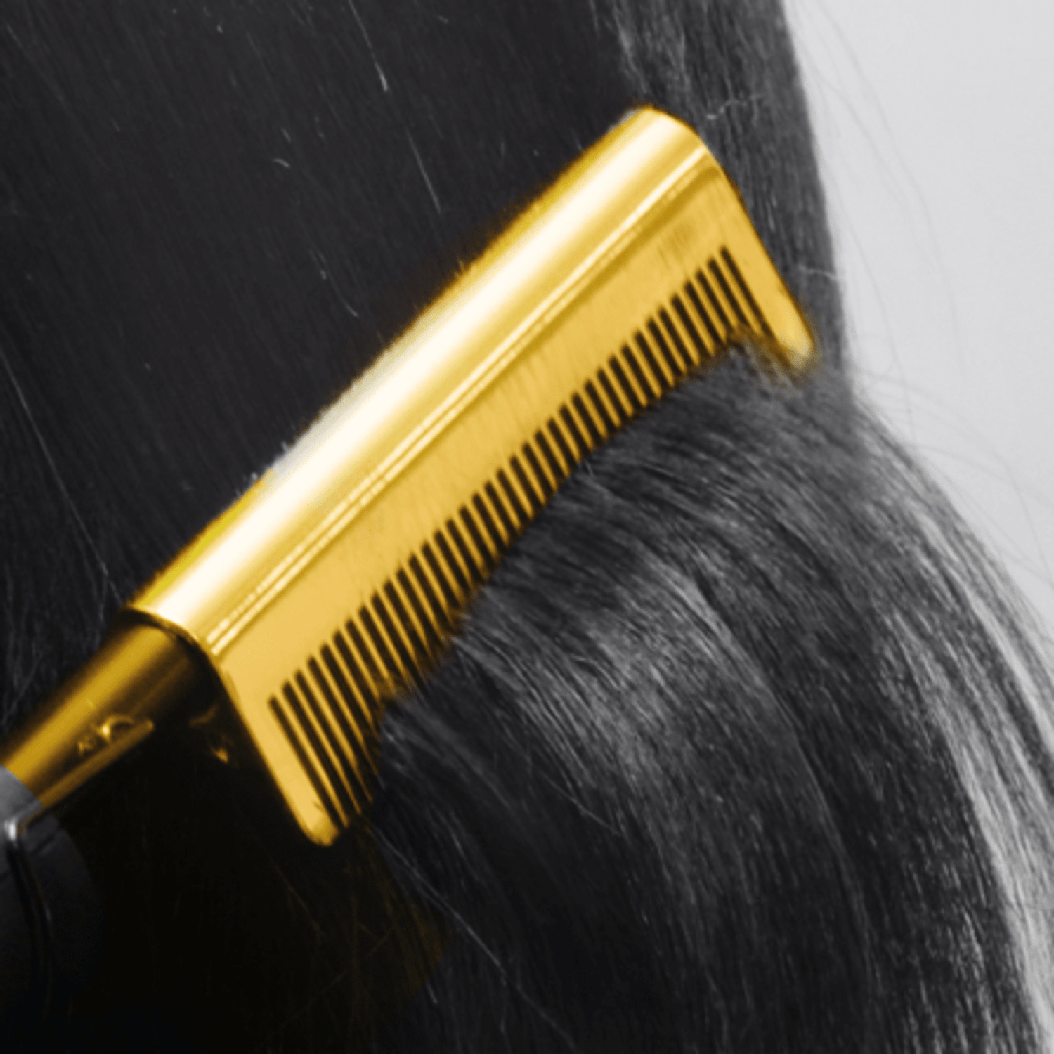 Gold-colored pressing comb gliding through smooth, straight black hair, showing fine, evenly spaced teeth for styling.