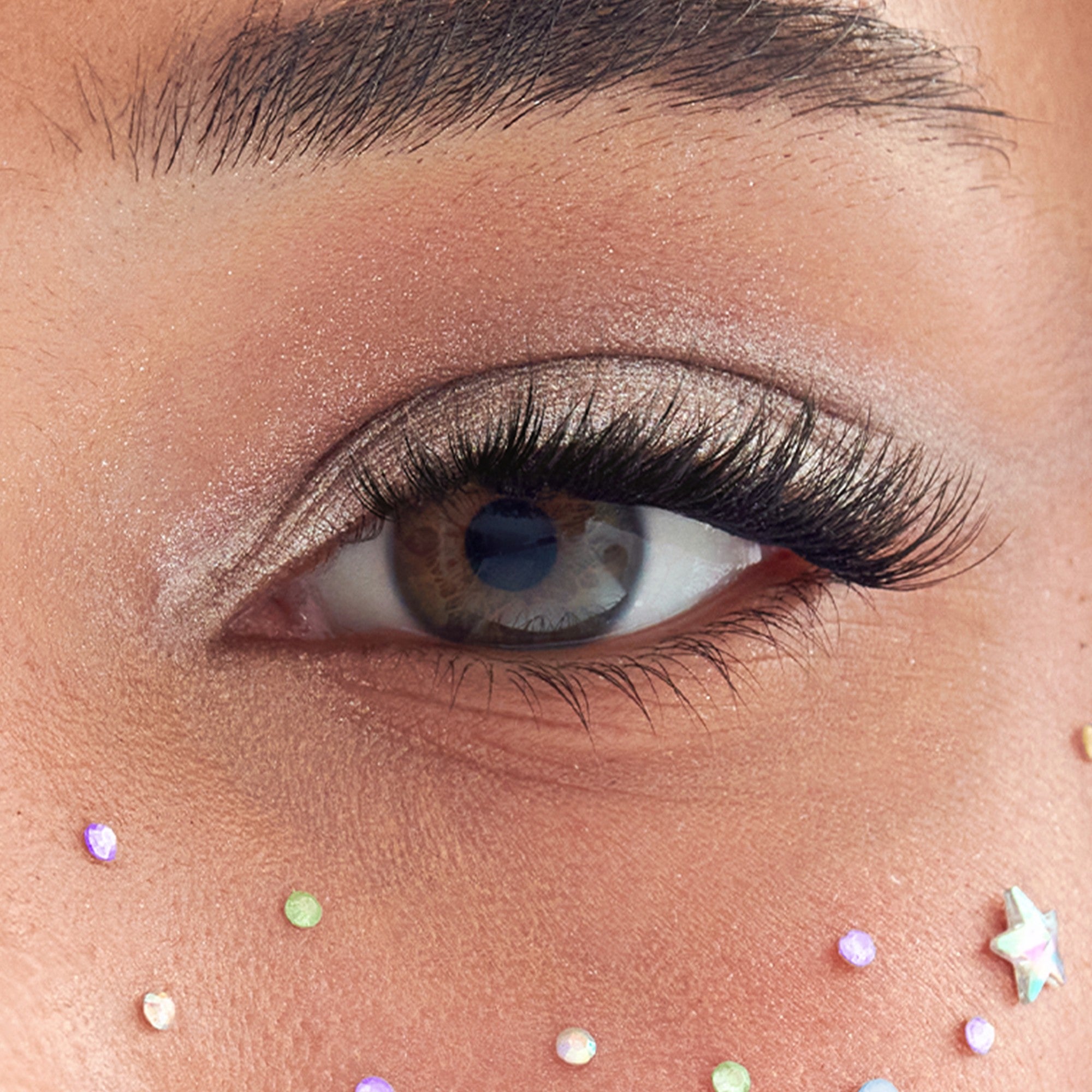 Close-up of eye with glittery eyeshadow and false lashes, face gems below.