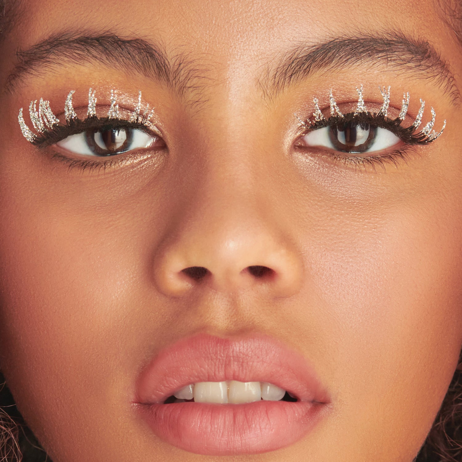 Close-up of face with glittery eyeshadow, defined brows, and pink lipstick.