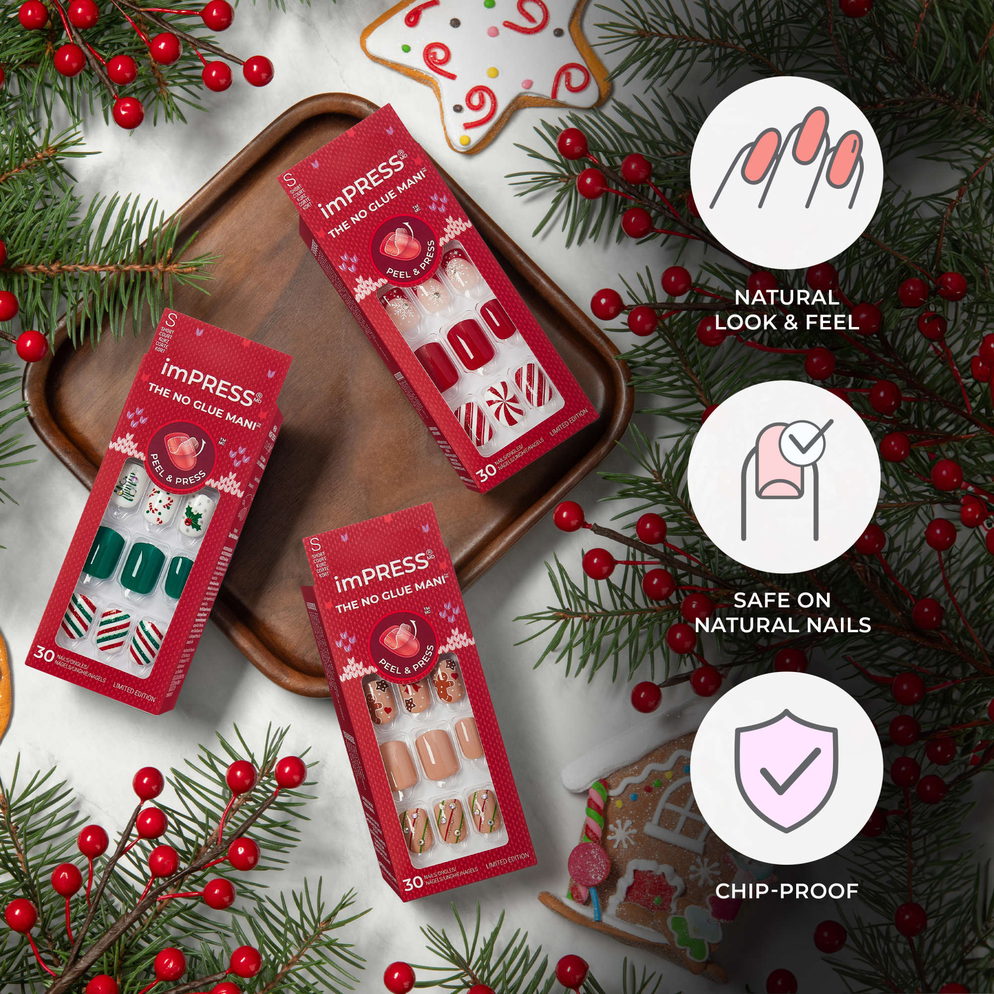 Three red-packaged imPRESS Press On Nails gift sets with holiday-themed nail designs on a wooden tray and marble surface, surrounded by festive greenery and cookies. Text highlights \