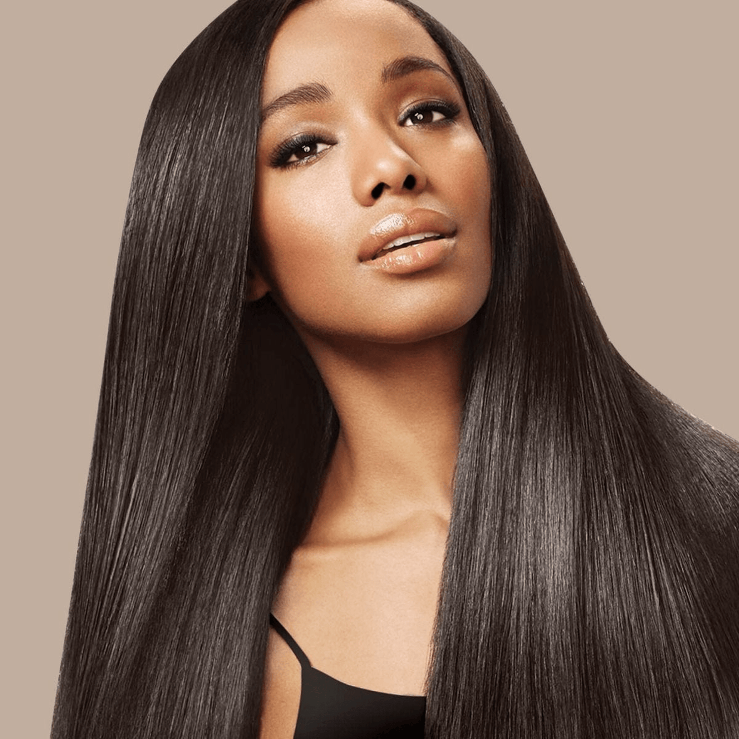 Woman with long, smooth, and shiny straight dark hair styled against a neutral beige background, showcasing sleek hair results.